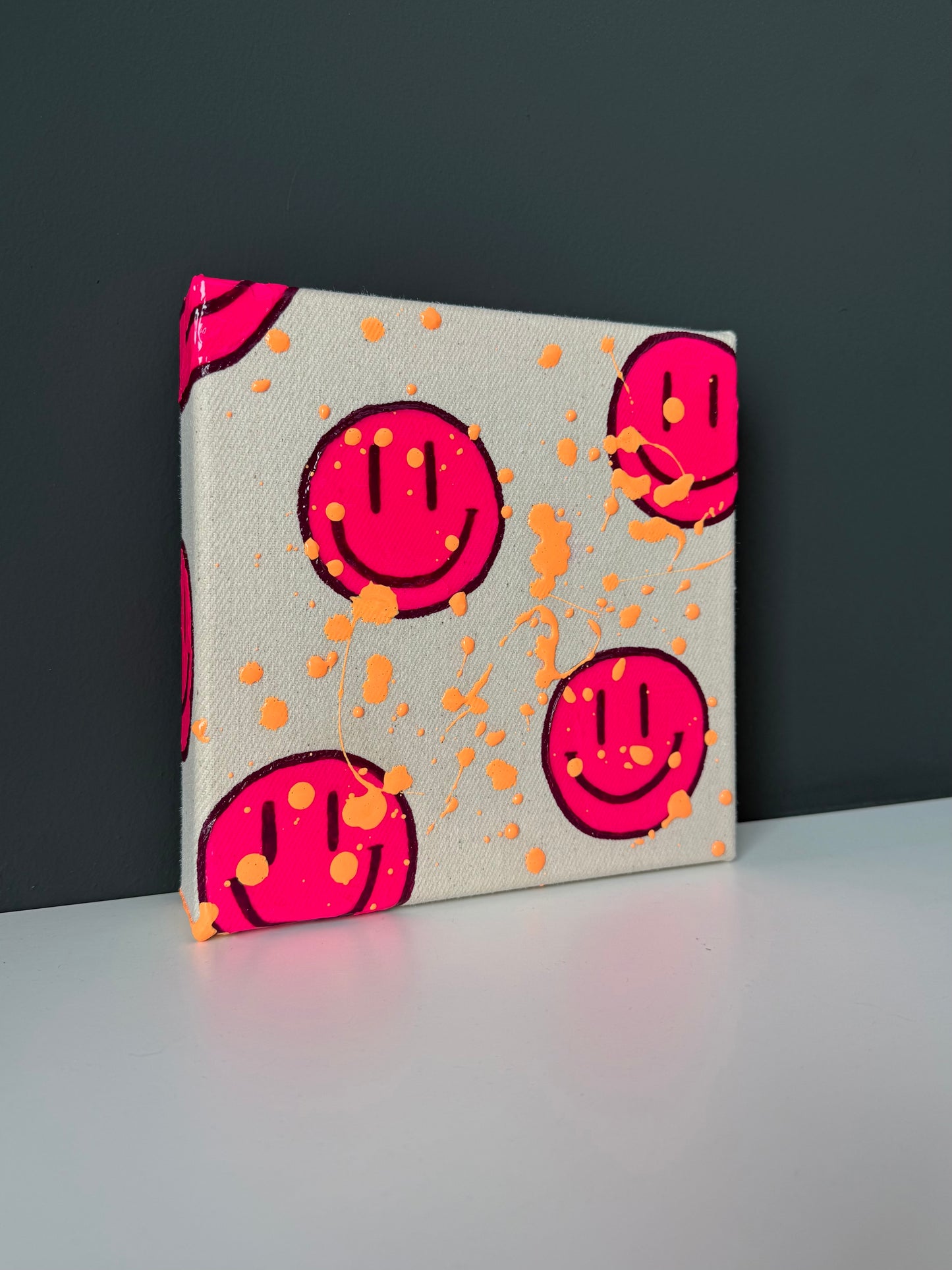 Smiley Acrylbild in Neonpink mit apricotfarbenen Spritzern auf weißem Sideboard – modernes Kunstwerk auf Leinwand aus der HAPPY Serie
