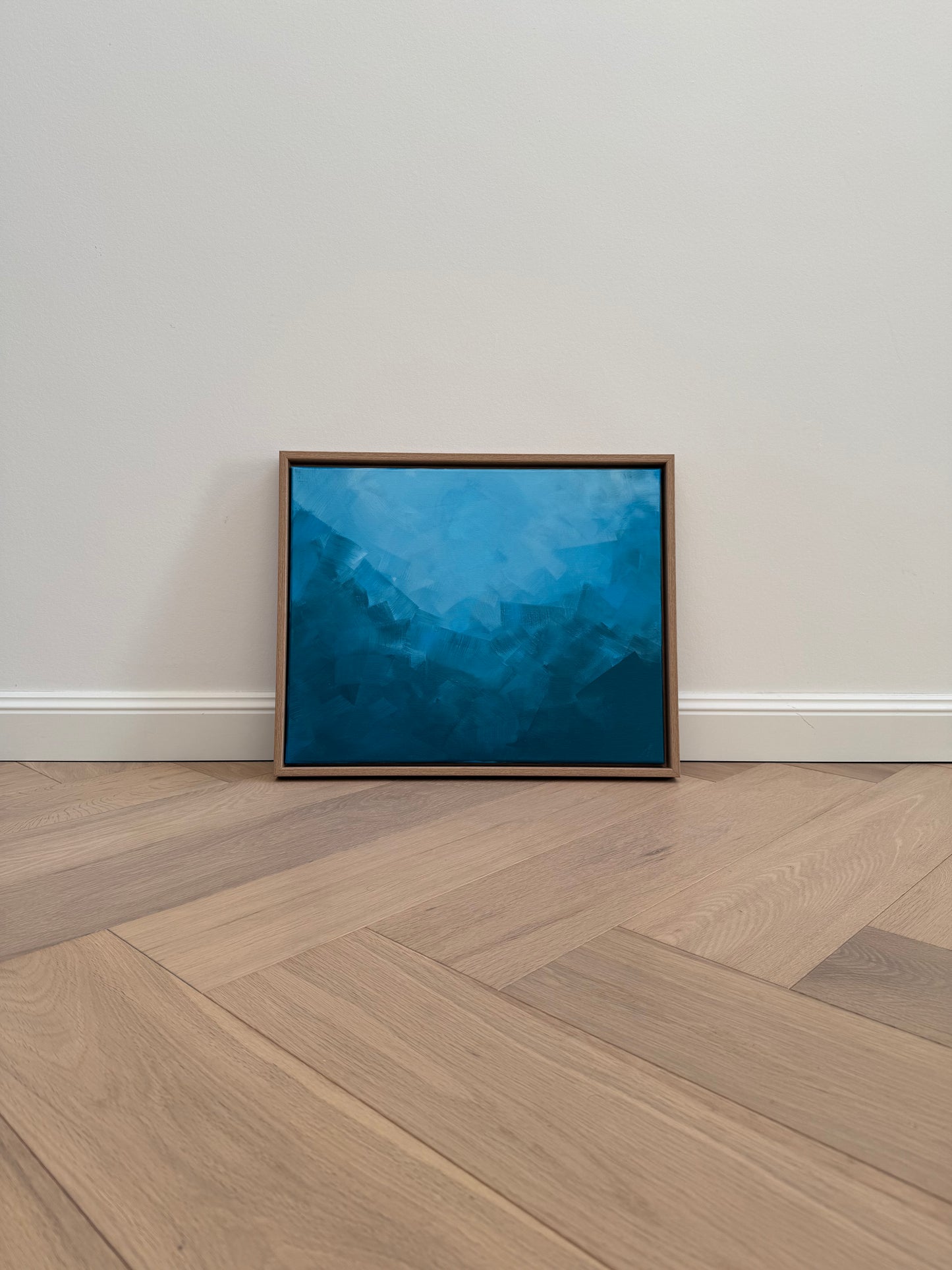 Abstraktes Acrylkunstwerk „BLUE“ in Blautönen, gerahmt in Naturholz, an heller Wand auf Holzboden platziert.