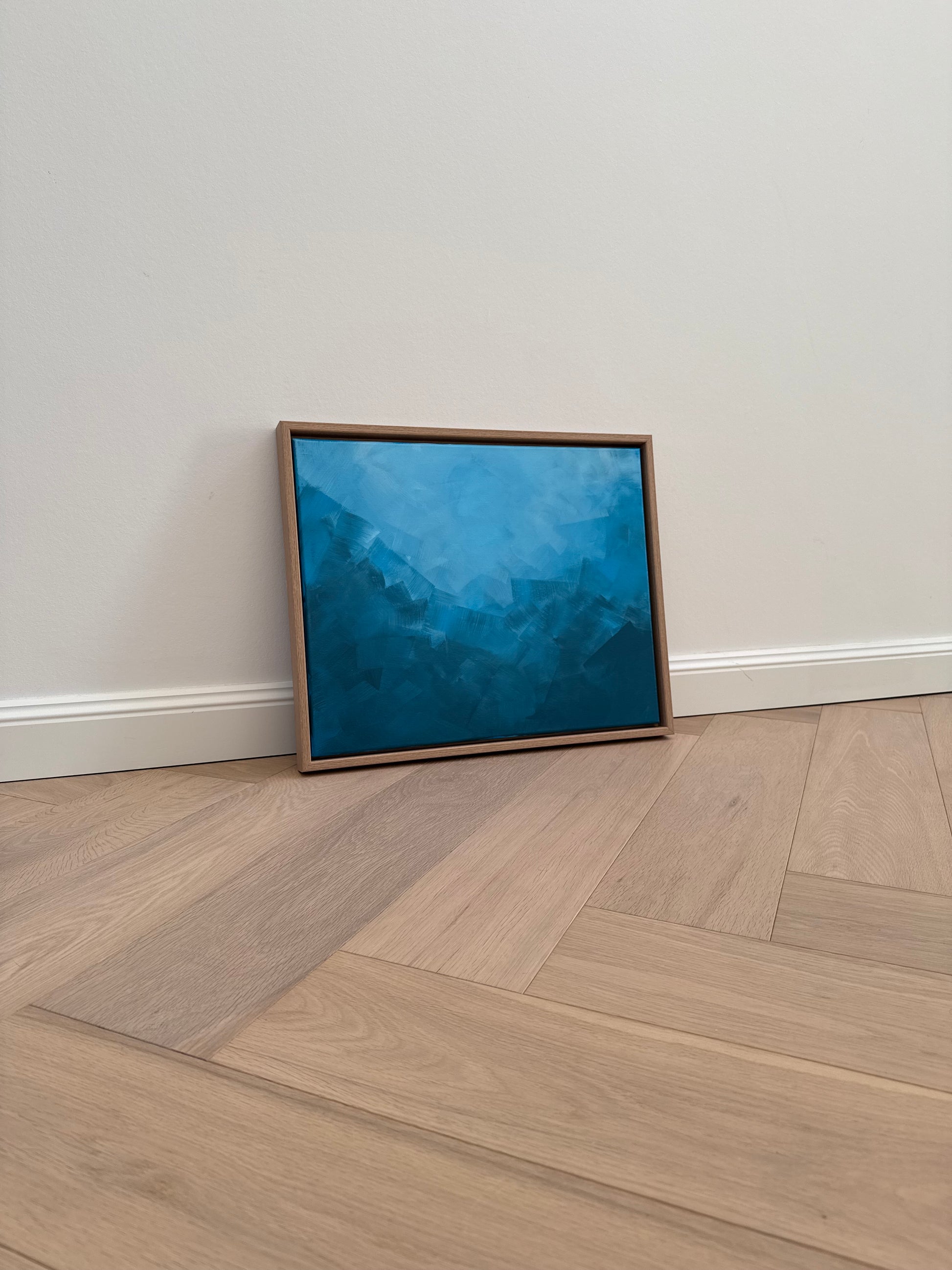 Abstraktes Acrylkunstwerk „BLUE“, seitliche Aufnahme, in verschiedenen Blau-Tönen, gerahmt in Eiche Natur, an weißer Wand auf Parkettboden platziert.