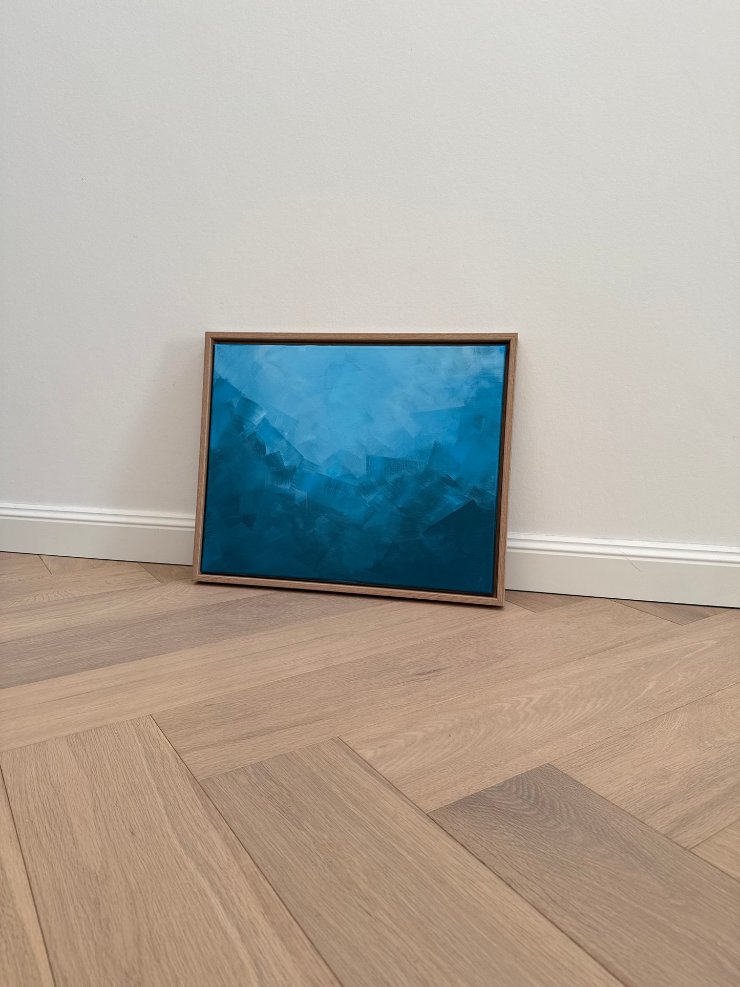 Abstraktes blaues Acrylbild in Holzrahmen vor heller Wand.