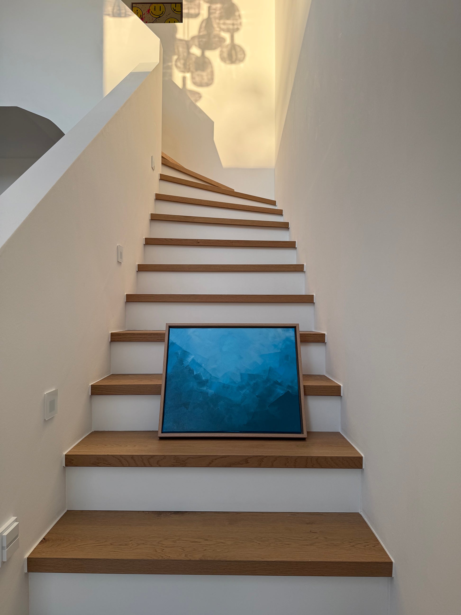 Ruhiges abstraktes Acrylgemälde in Blautönen, gerahmt in Holz, inszeniert auf einer modernen Holztreppe.