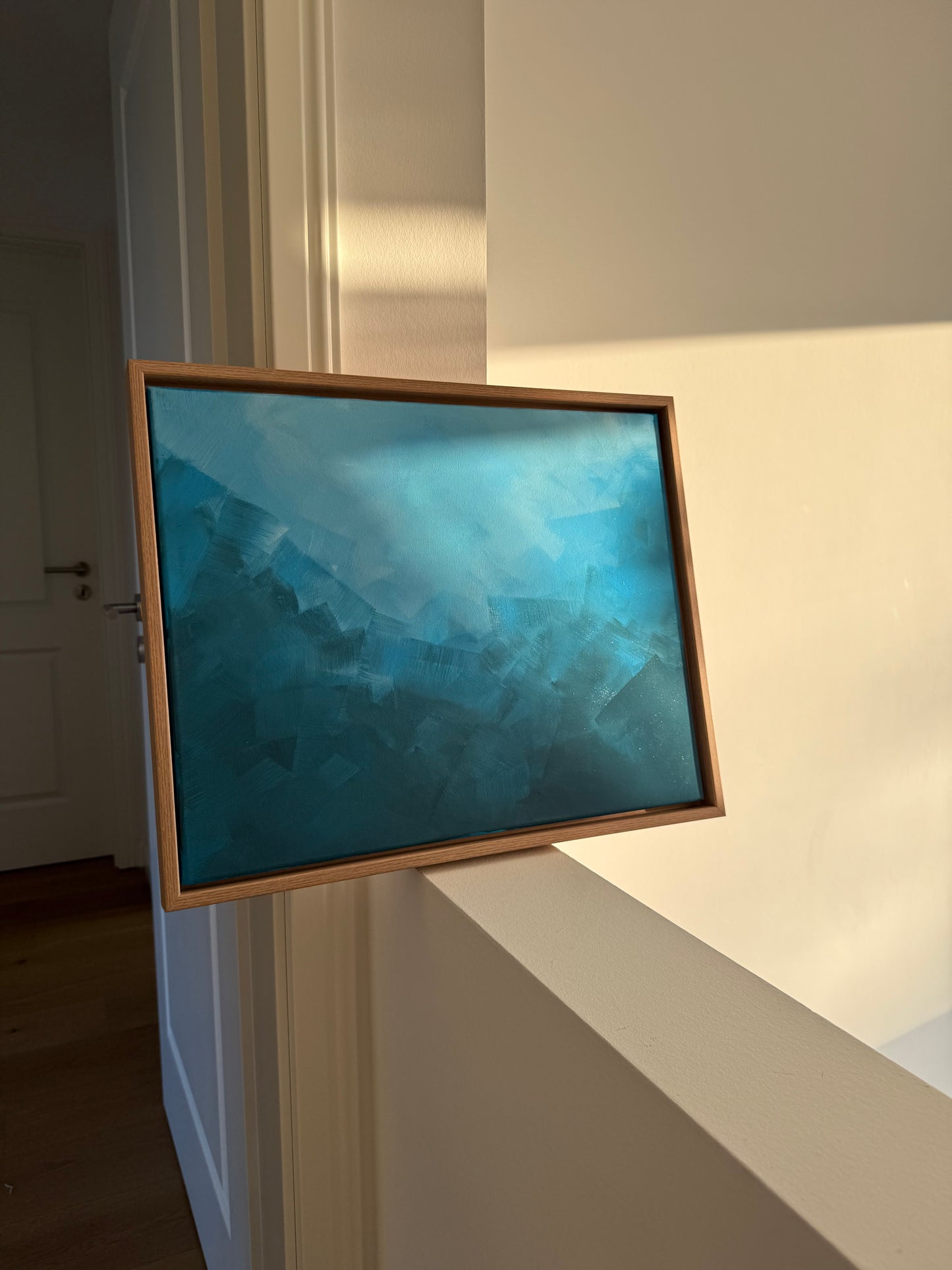 Abstraktes Acrylkunstwerk „BLUE“ in Blautönen, gerahmt in Naturholz, im warmen Abendlicht – schimmernde Farben und feine Oberflächenstruktur.