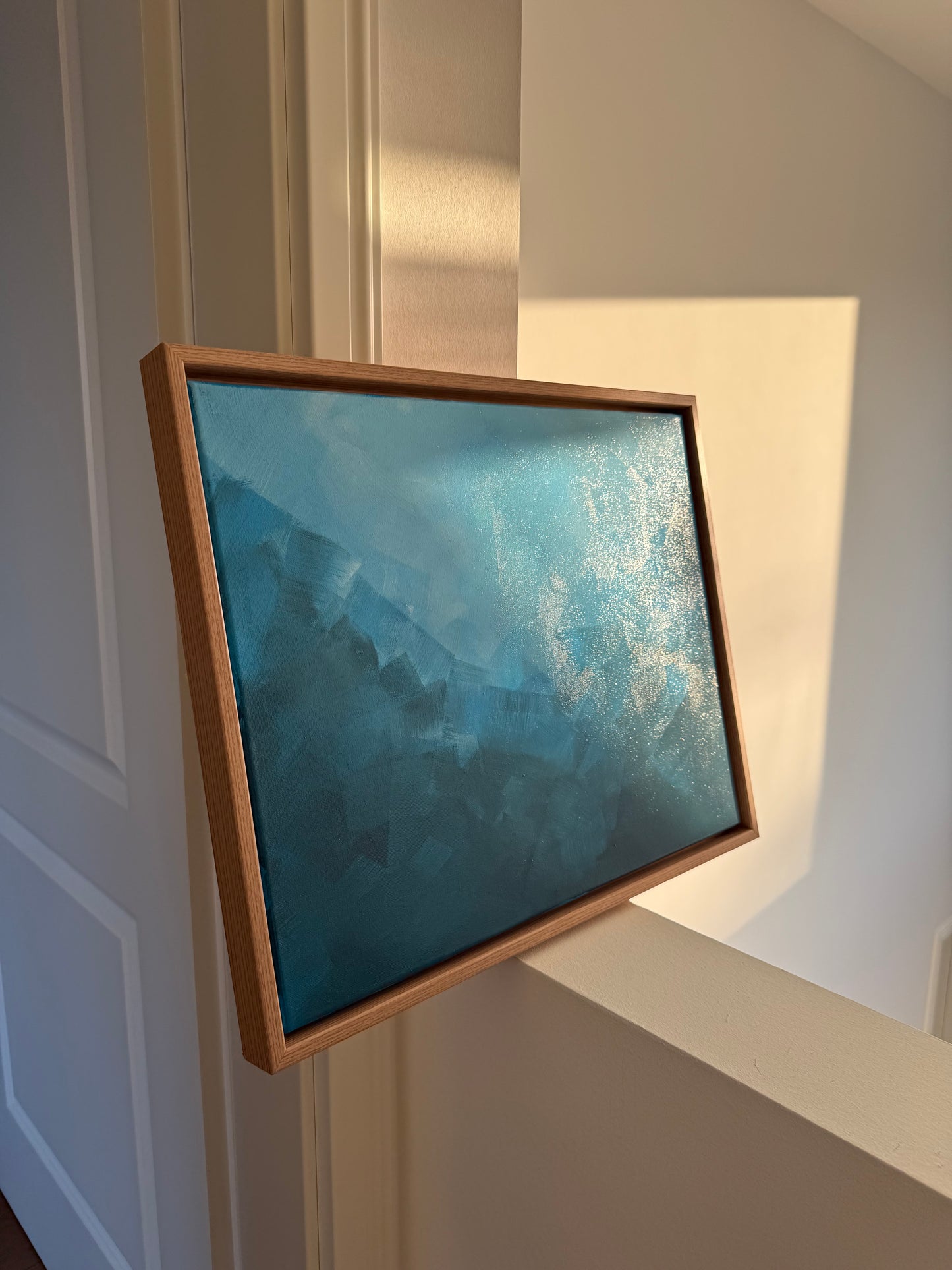 Abstraktes blaues Acrylbild im Holzrahmen, dessen Farben und Textur im Abendlicht schimmern.