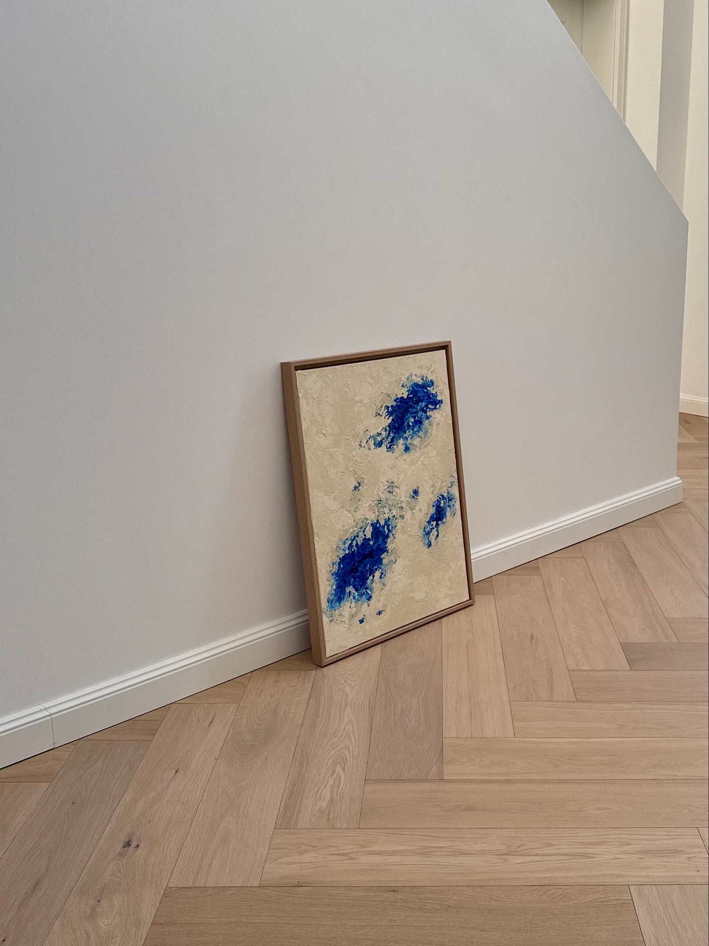 Strukturiertes abstraktes Acrylbild in Beige und Blau mit vielschichtiger Oberfläche und sanfter Bewegung auf hellem Holzboden vor weißer Wand