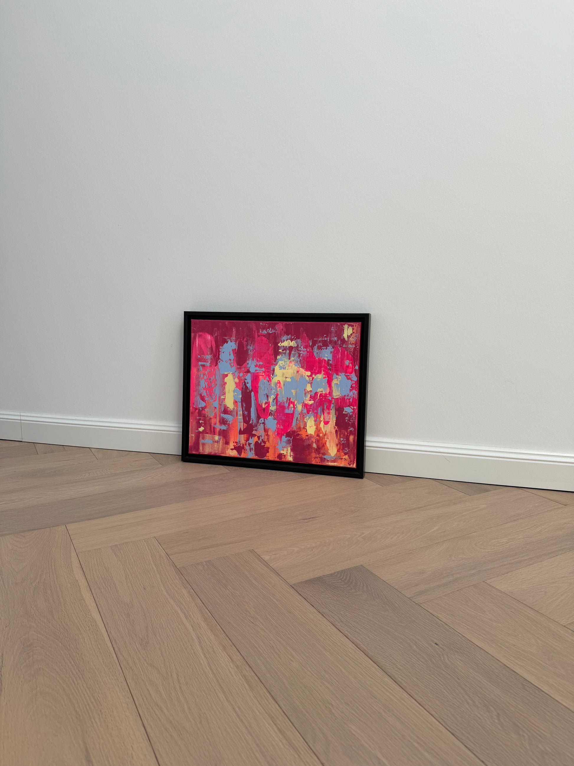Abstraktes Originalkunstwerk „EVOLVING“ in Pink, Blau, Orange und Gelb, Acryl auf Leinwand, im schwarzen Rahmen an heller Wand auf Holzboden