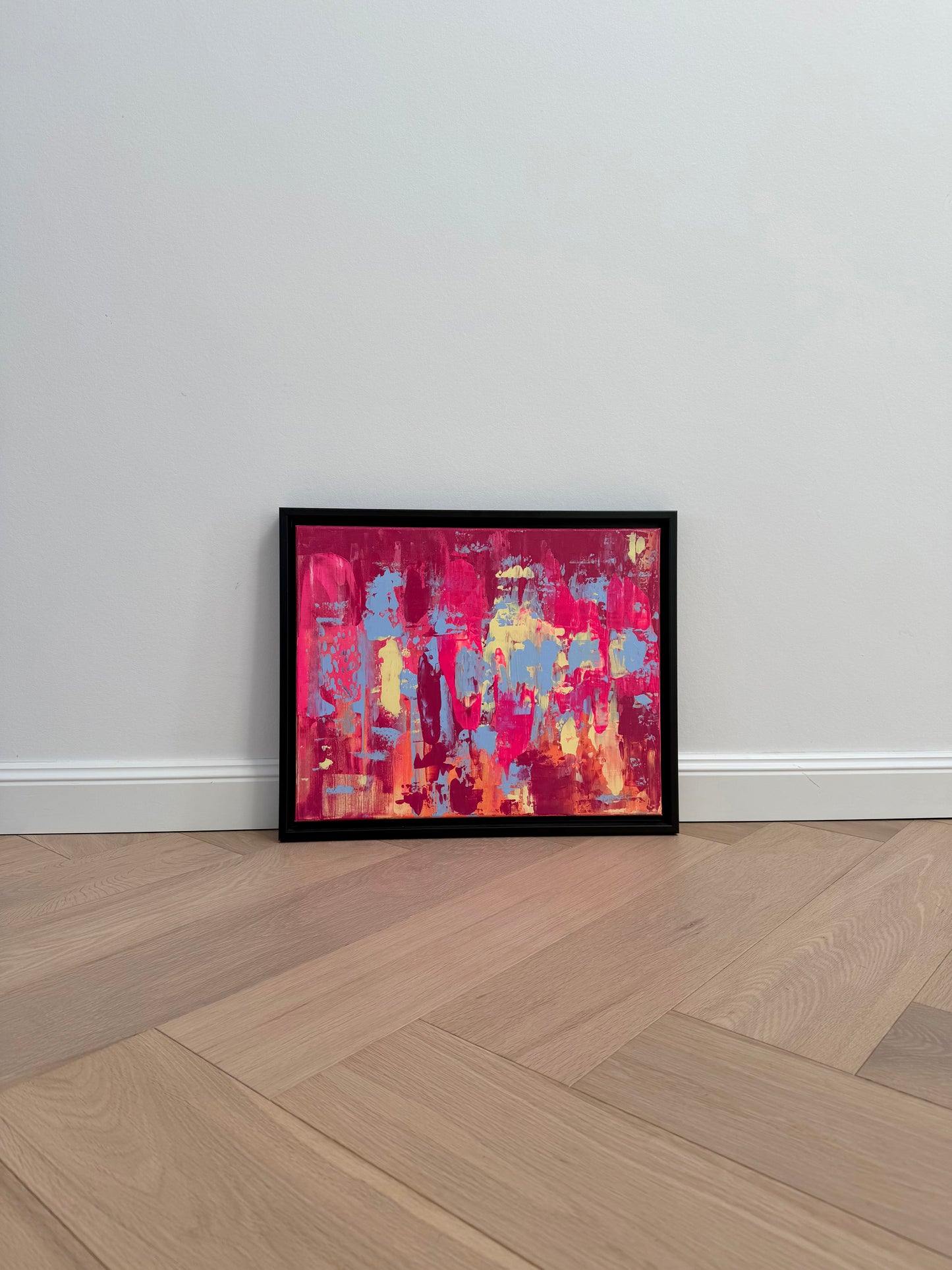 Abstraktes Originalkunstwerk „EVOLVING“ in Pink, Blau, Orange und Gelb, Acryl auf Leinwand, im schwarzen Rahmen an heller Wand