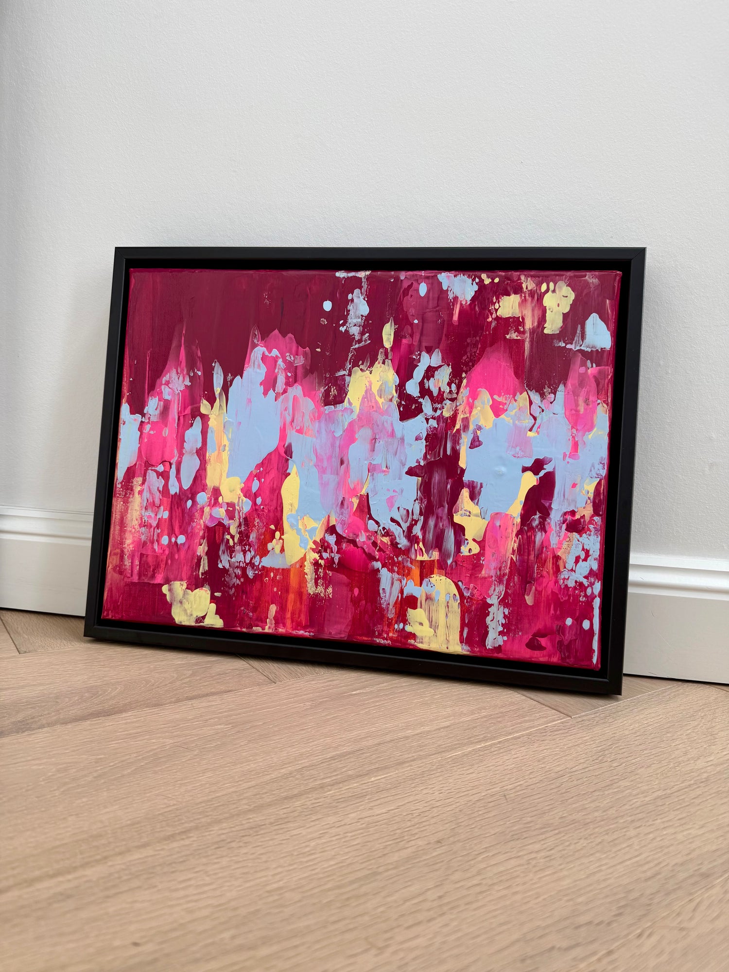 Abstraktes Acrylgemälde EVOLVING #2 in Pink, Magenta, Blau, Orange und Hellgelb, gerahmt in Schwarz auf hellem Boden vor weißer Wand