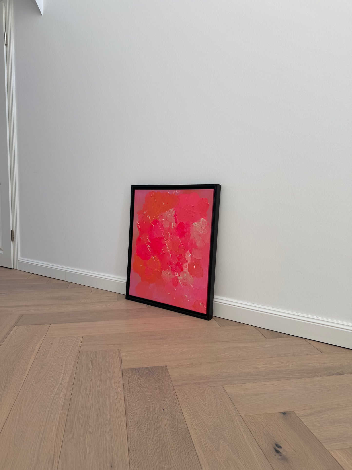 Abstrakte Kunst in Pink und Orange mit strukturierter Oberfläche und Glanz, gerahmt in schwarzem Holzrahmen auf Holzparkett
