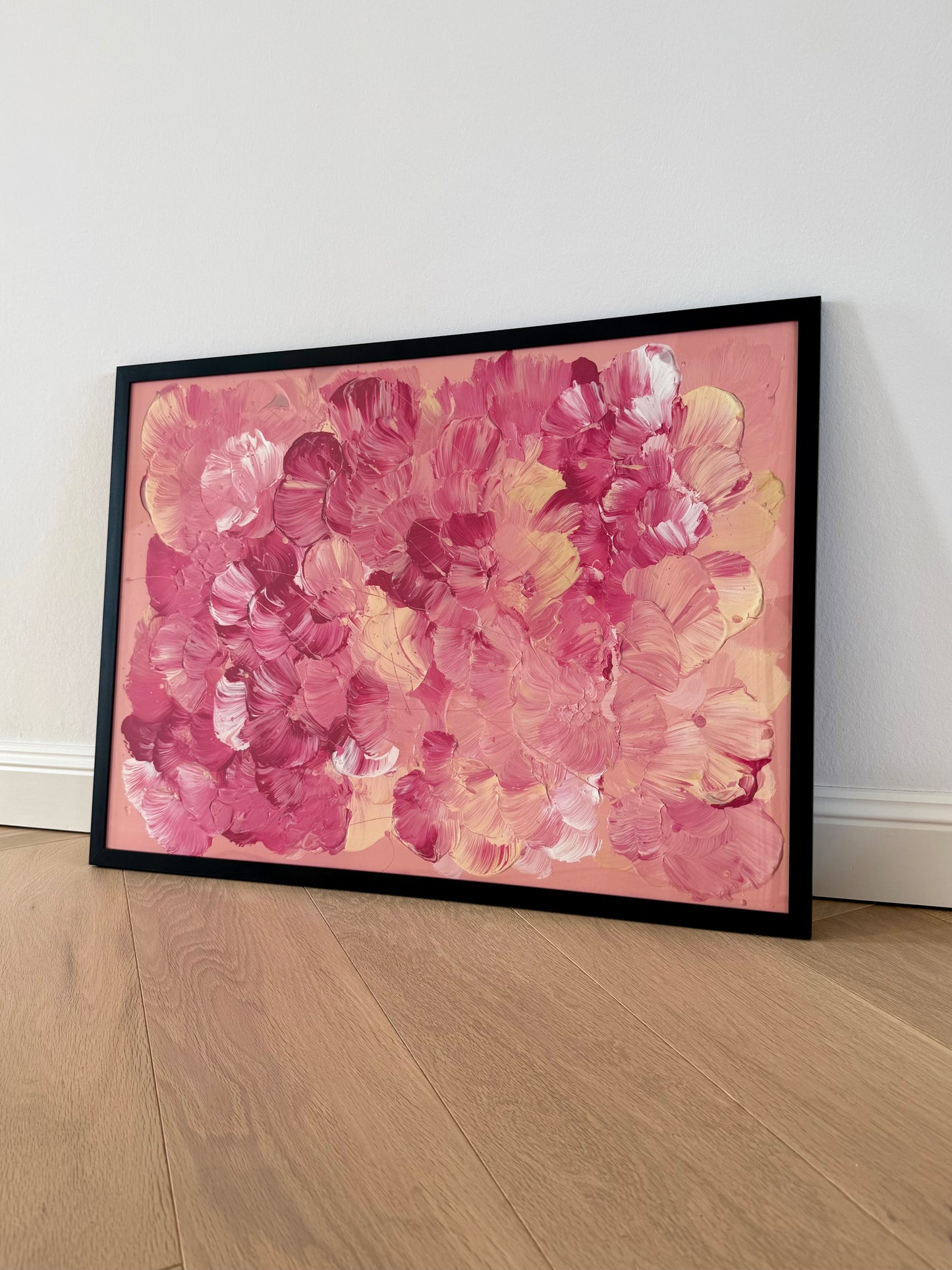 Gerahmter Fine Art Print FLORALS #18 lehnt an einer hellen Wand auf Holzboden. Abstrakte Blütenformen in Rosa, Beere, Sand und Off-White füllen das Querformat.
