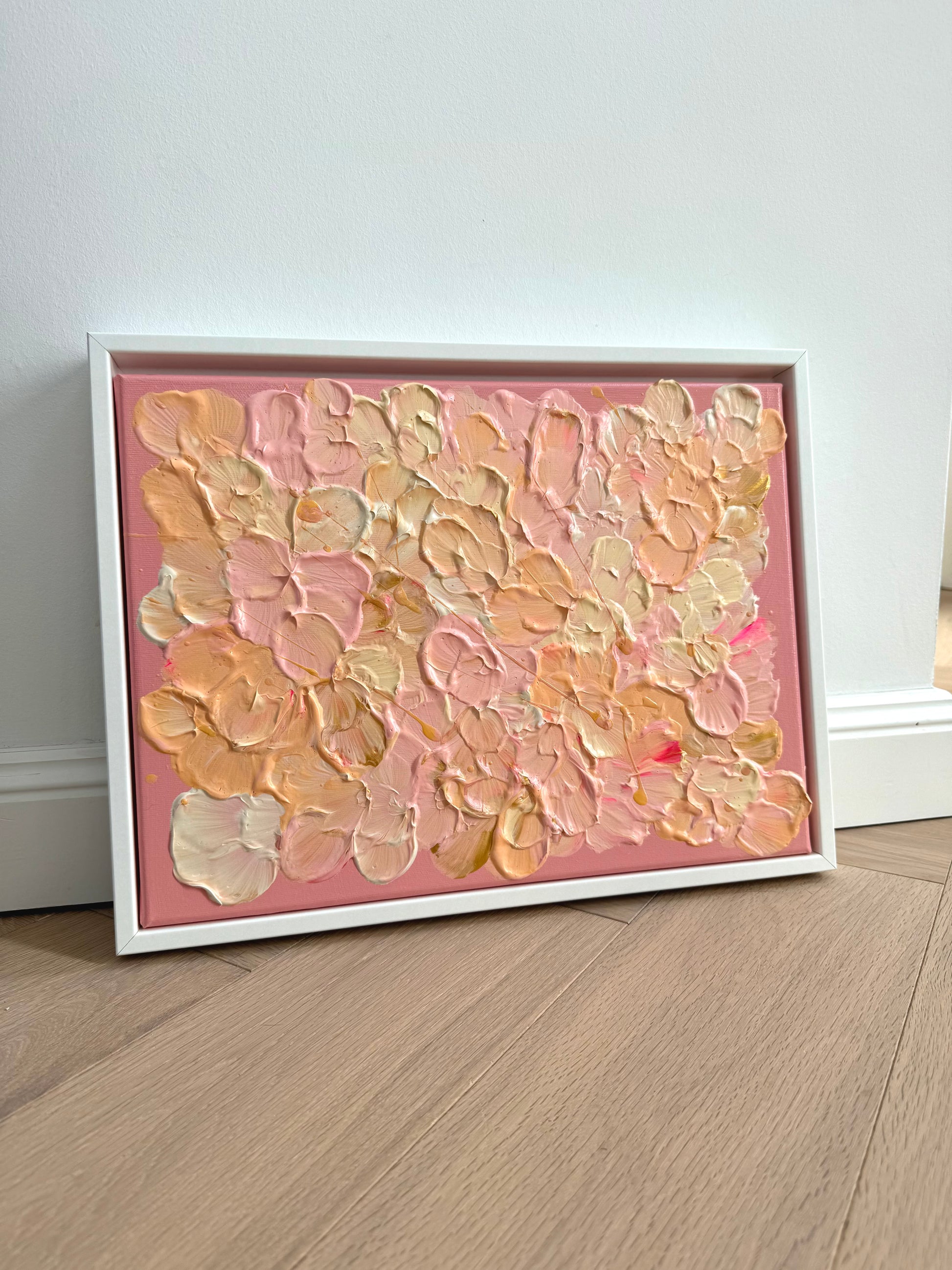 Gerahmtes Acrylbild FLORALS #19 im Querformat, angelehnt an eine helle Wand, mit floraler Textur in Rosa, Apricot und Buttergelb.