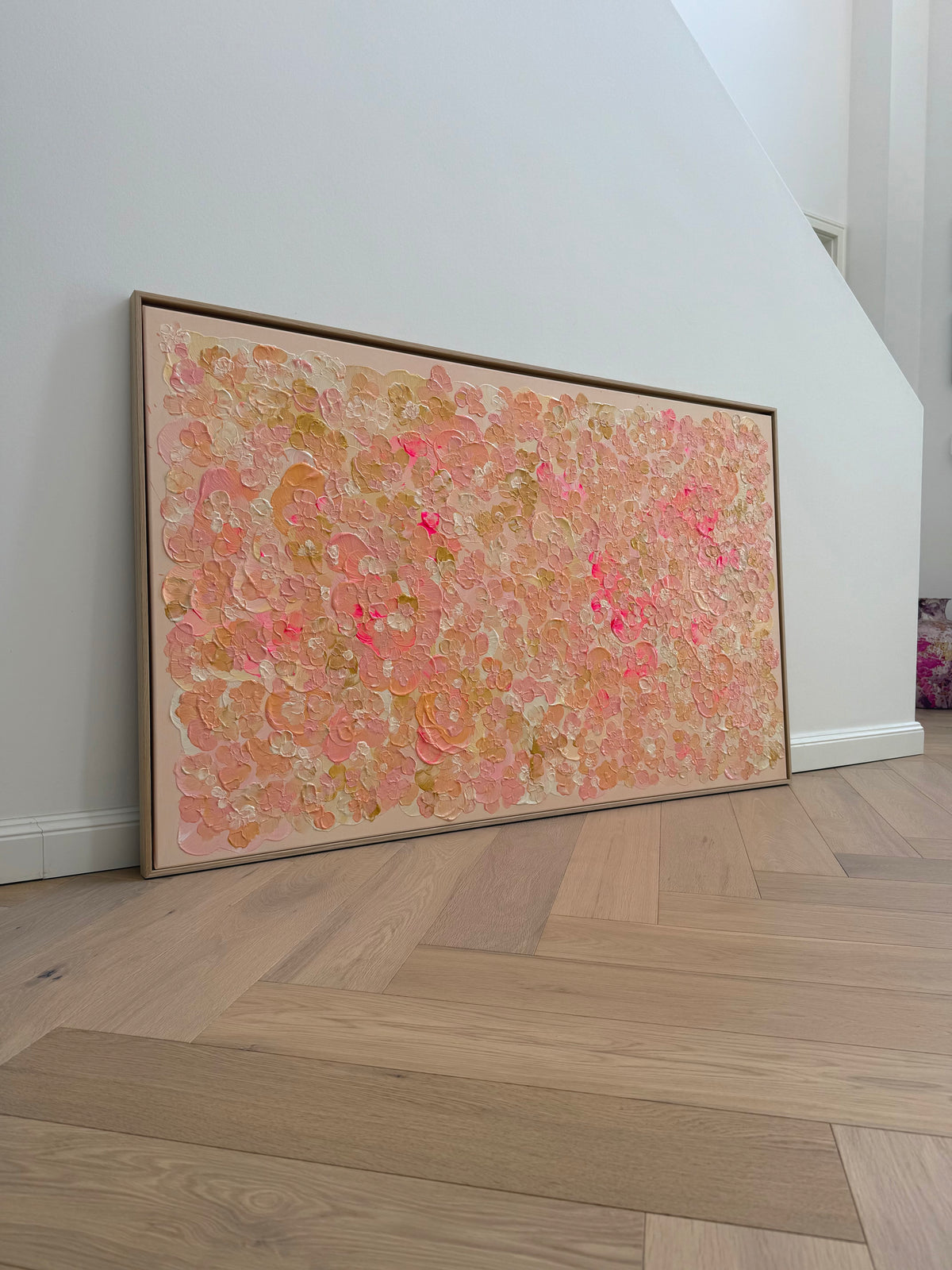 Großformatiges Auftragskunstwerk FLORALS #23 von Sophia Toschka, 150 × 90 cm, angelehnt an eine helle Wand auf Holzboden, mit floraler Struktur in Rosa, Apricot, Creme und Neonpink im hellen Holzrahmen.
