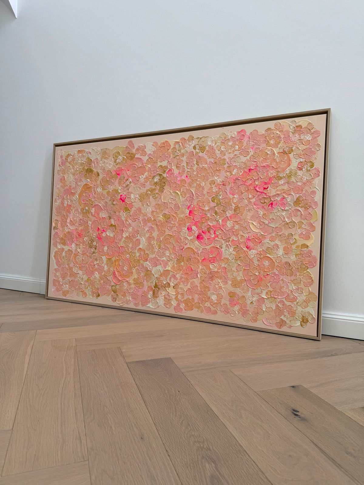 Schräg fotografiertes Auftragskunstwerk FLORALS #23 auf hellem Holzboden. Die abstrakten Blütenformen in Rosa, Apricot, Creme und Pink entfalten sich über das großformatige Querformat.