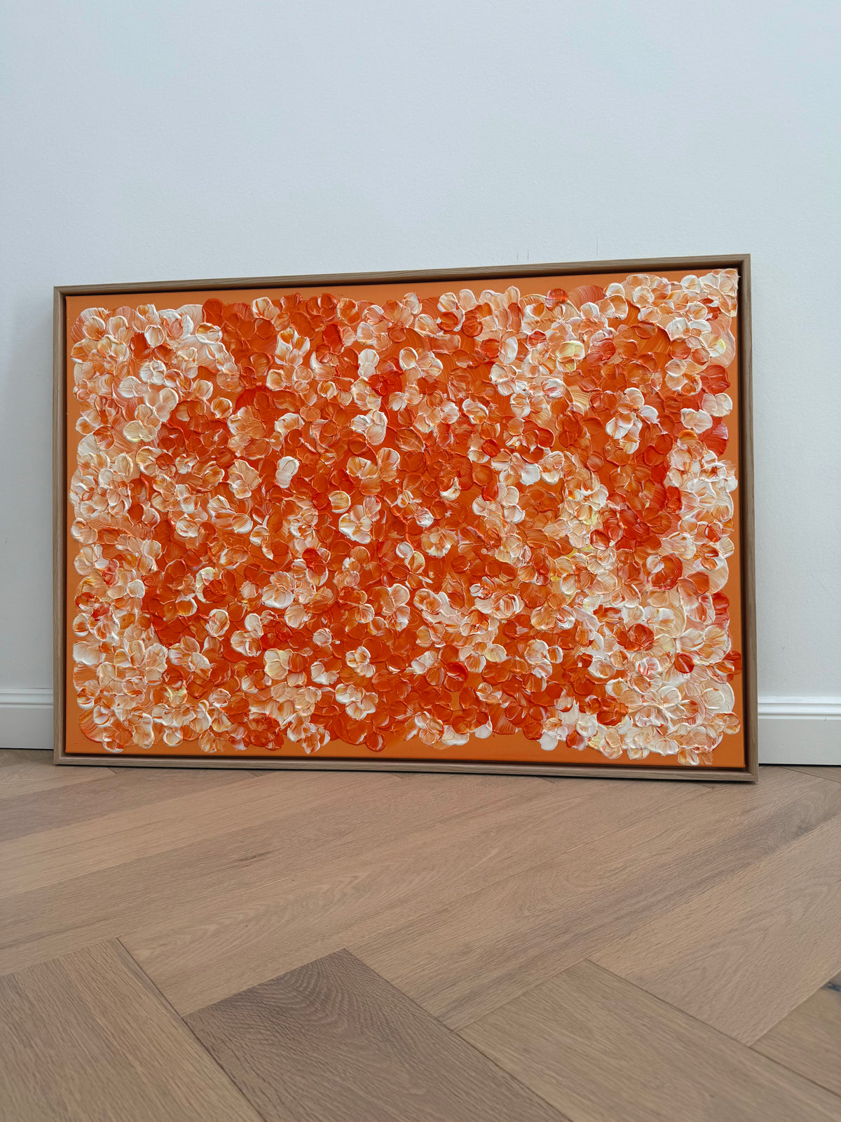 Nahezu frontale Ansicht von FLORALS #25, einem Kunstwerk mit dichten orangefarbenen und cremeweißen Blütenformen, gerahmt im Schattenfugenrahmen aus Eiche Natur auf hellem Holzboden.