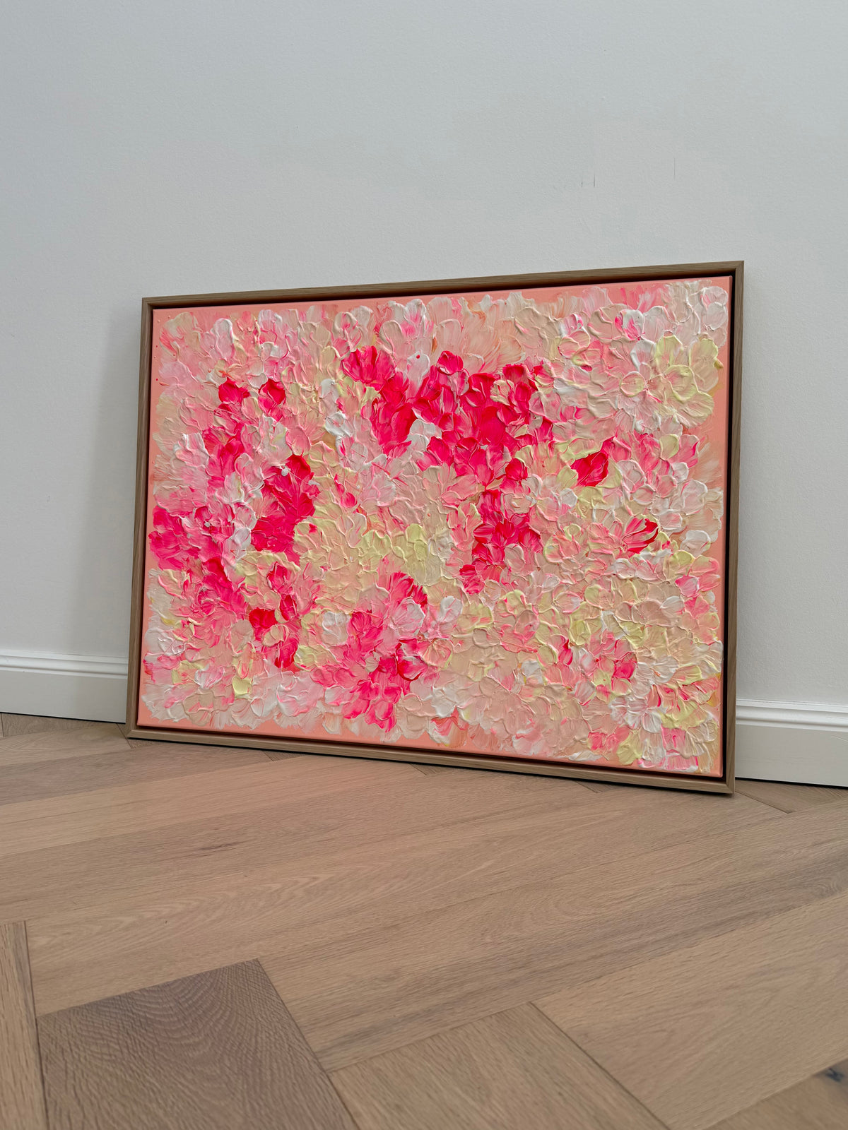 FLORALS #26, florales Acrylbild in Neonpink, Creme und Hellgelb auf apricotrosa Grund, 80 × 60 cm, gerahmt in heller Eiche Natur.