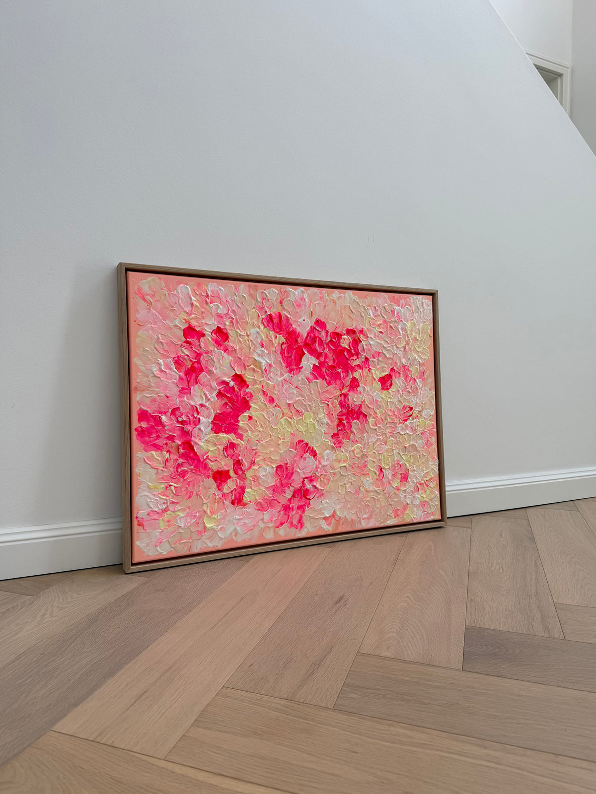 FLORALS #26 an einer weißen Wand auf hellem Holzboden, mit neonpinken Blütengruppen zwischen cremefarbenen und hellgelben Formen im Eichenrahmen.