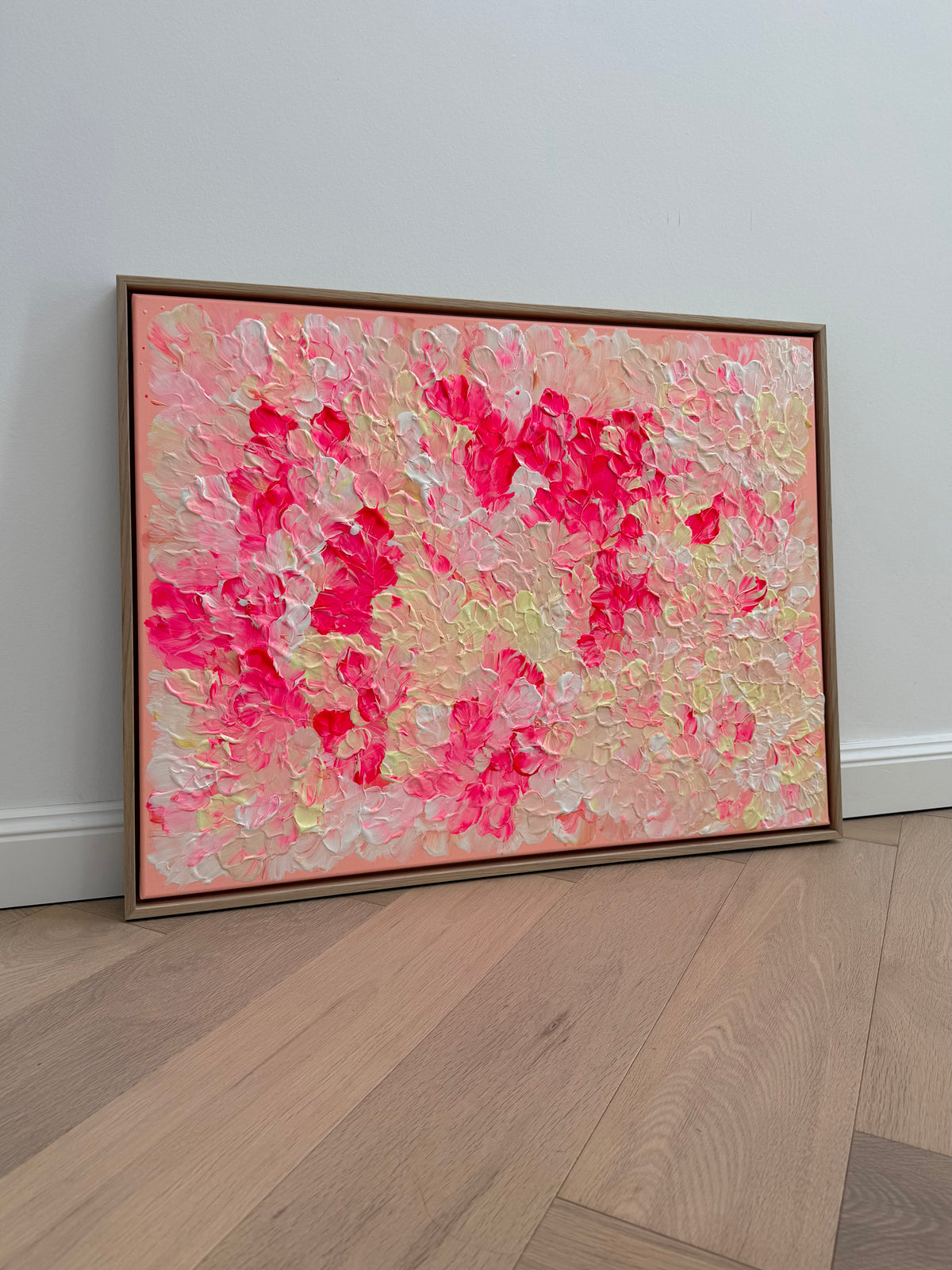 Schrägansicht von FLORALS #26 mit plastischen Blütenformen in Neonpink, Nude und Creme auf warmem Apricotrosa, eingefasst von einem hellen Schattenfugenrahmen.
