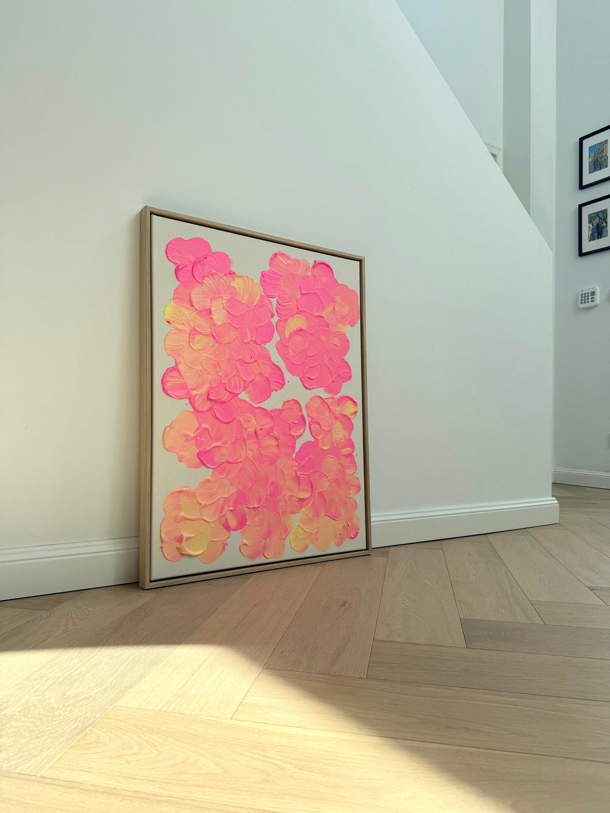 FLORALS #27 an einer hellen Wand mit Sonnenlicht auf dem Holzboden, großflächige pinke und lachsorangefarbene Blüten im Schattenfugenrahmen aus Eiche Natur.