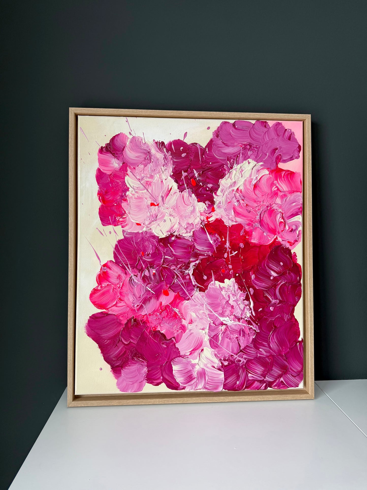 Abstrakte florale Malerei in kräftigem Pink und Burgunder vor dunkler Wand präsentiert. Glänzendes Acrylbild mit strukturreicher Oberfläche als moderne Wanddekoration.