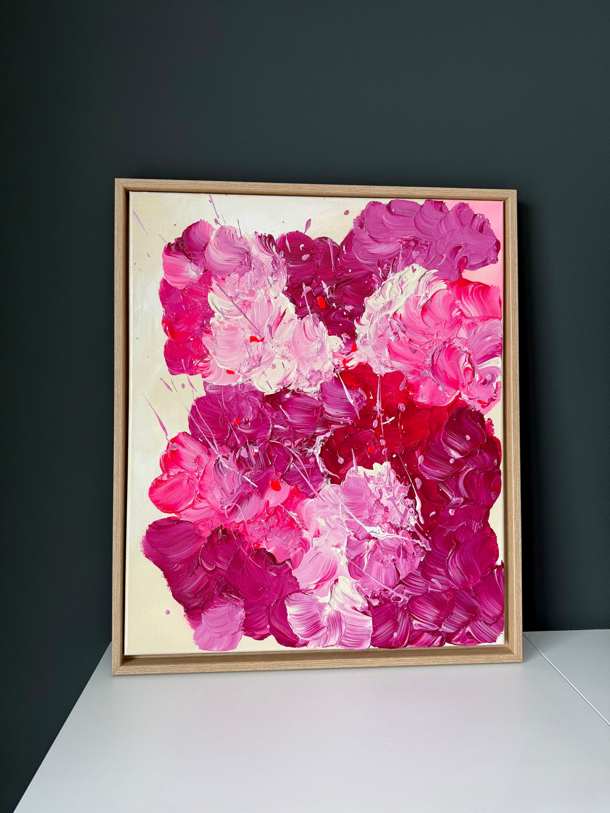Abstrakte florale Malerei in kräftigem Pink und Burgunder vor dunkler Wand präsentiert. Glänzendes Acrylbild mit strukturreicher Oberfläche als moderne Wanddekoration.