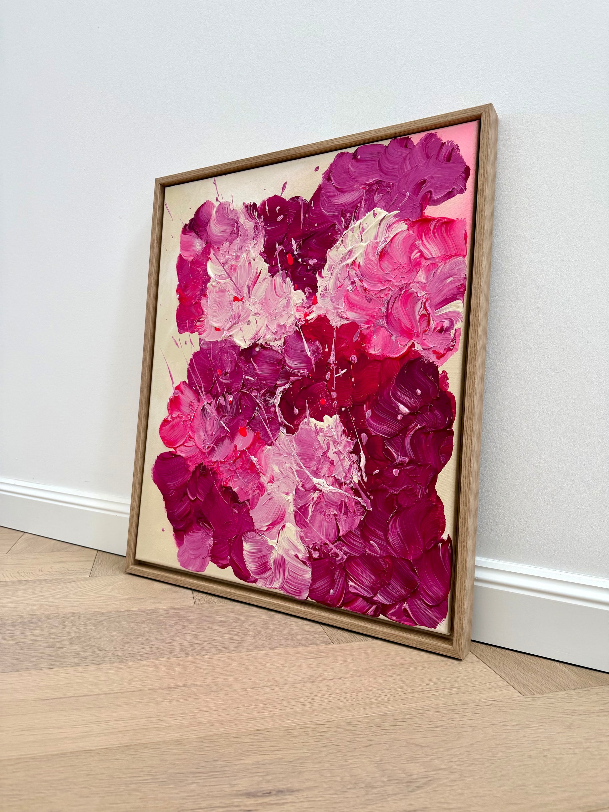 Abstraktes Acrylbild in Pink und Burgunder leicht angewinkelt auf hellem Parkettboden inszeniert. Glänzende Oberfläche und dynamische, florale Komposition.