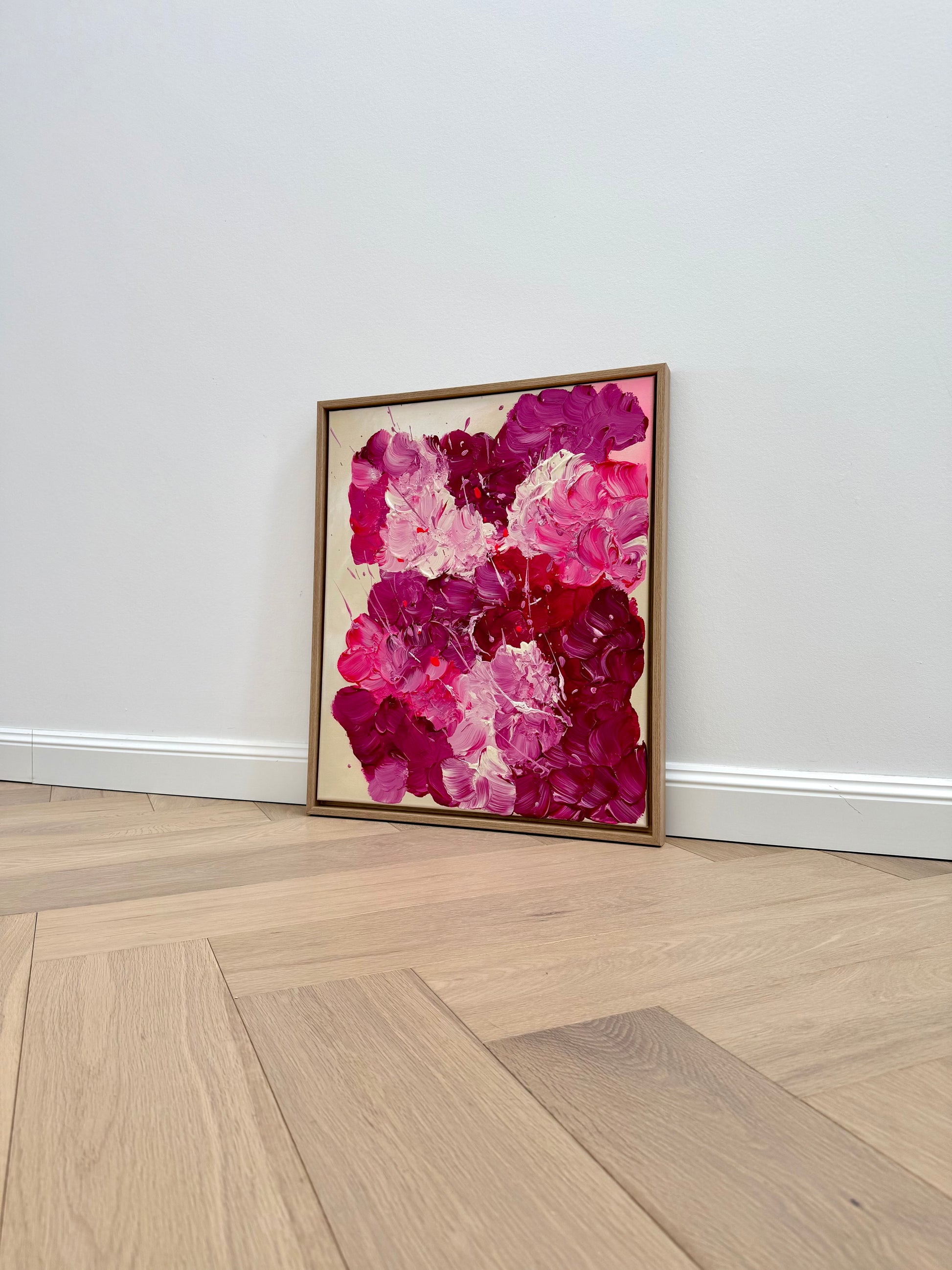 Abstraktes Blumenbild in 50x60 cm im Eiche-Rahmen, leicht schräg an eine helle Wand gestellt. Moderne florale Wandkunst mit kräftigen Pink- und Burgundertönen für stilvolle Wohnräume.