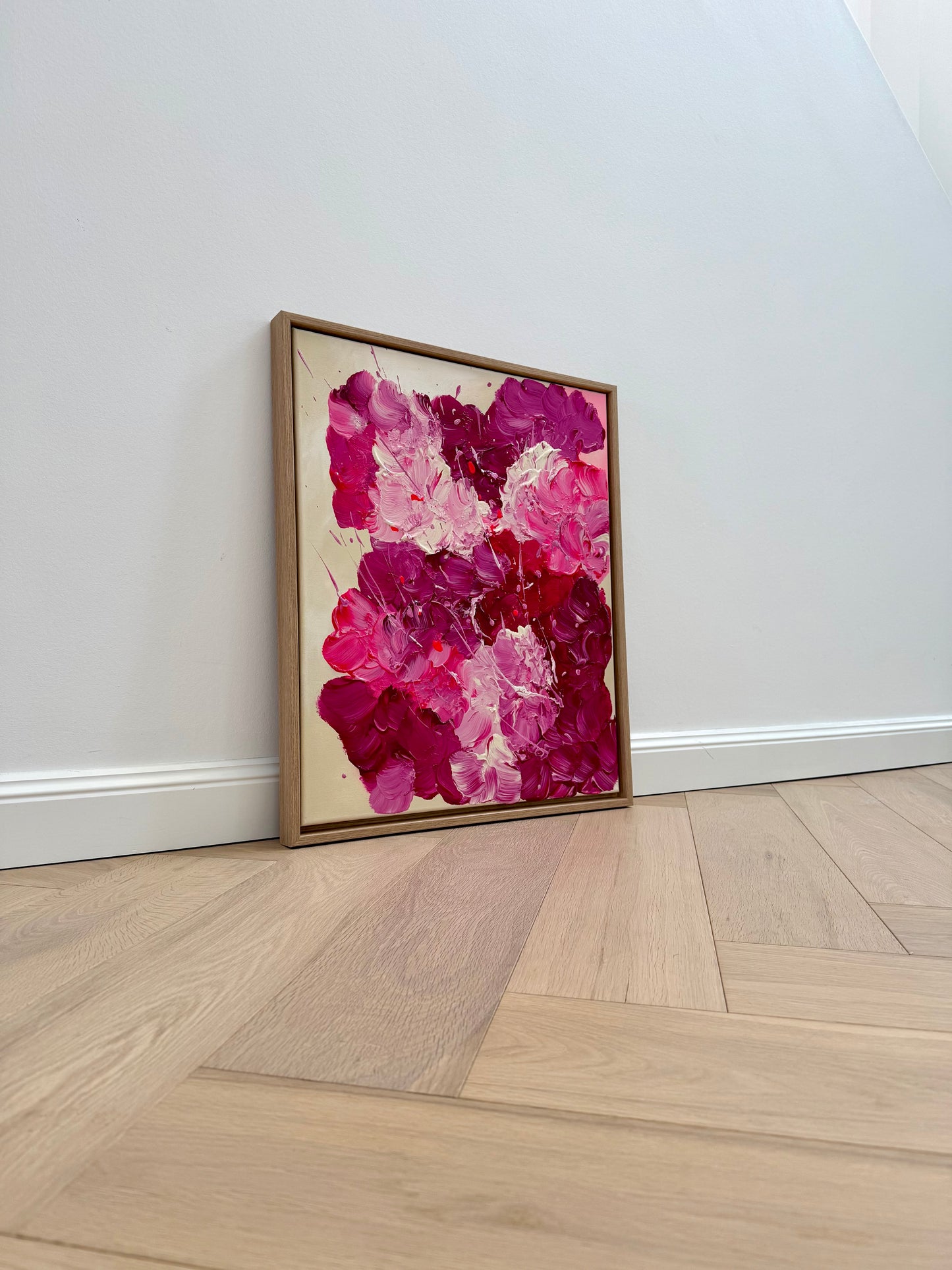 Modernes Acrylbild mit floraler Bewegung, im Eiche-Rahmen an heller Wand aufgestellt. Ausdrucksstarke Wandkunst in Pink und Burgunder für Wohnzimmer oder Schlafzimmer.
