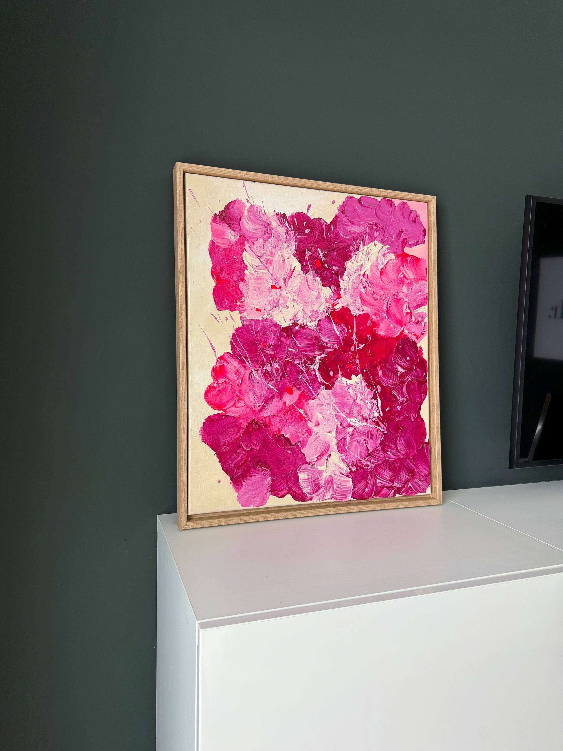 Abstraktes florales Gemälde in Pink und Burgunder auf schmaler Konsole vor dunkler Wand. Moderne Wandkunst mit glänzender Oberfläche und emotionaler Farbtiefe.