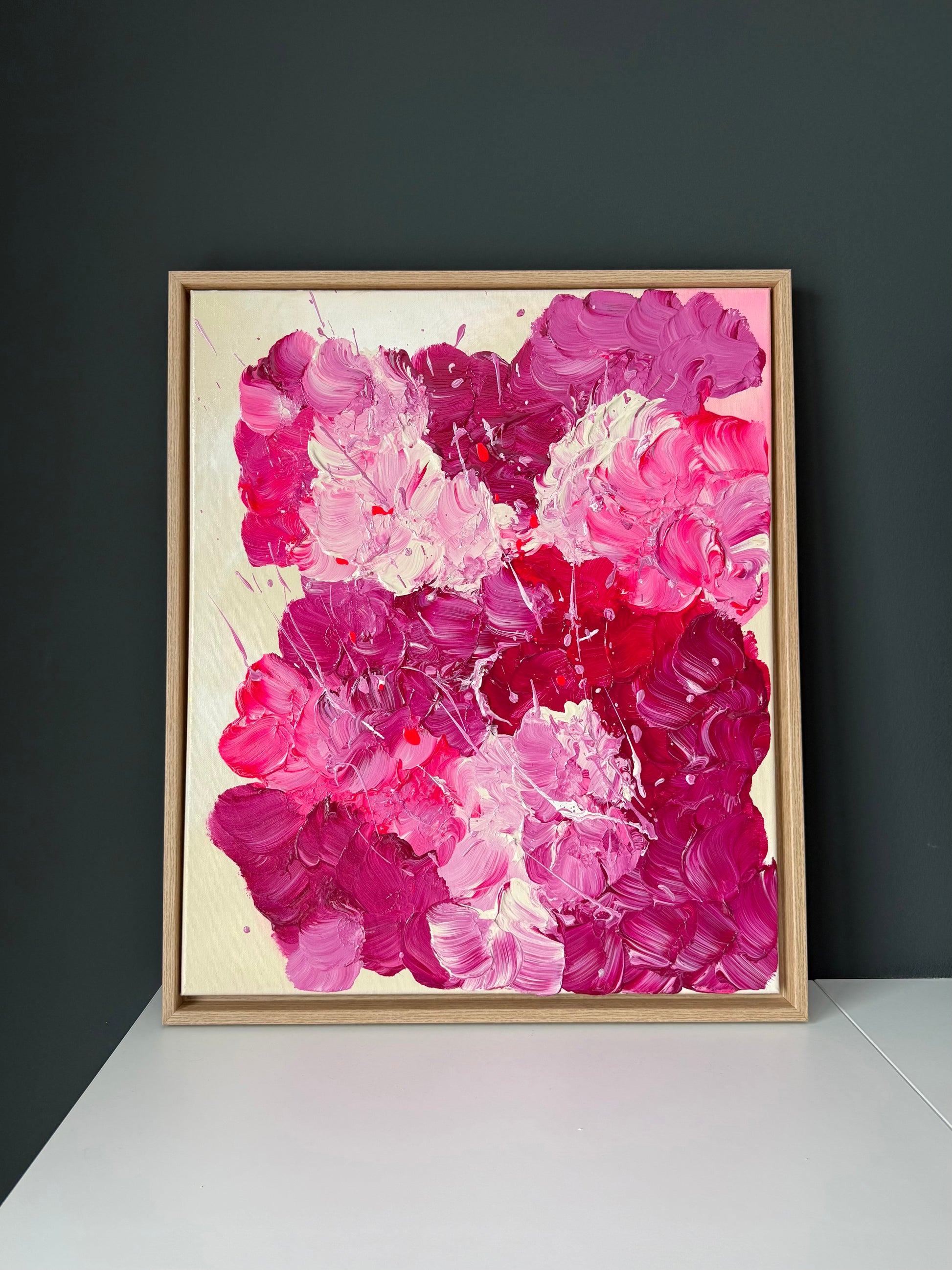 Abstrakte florale Wandkunst in kräftigem Pink im Eiche-Schattenfugenrahmen vor dunkler Akzentwand. Strukturreiches Acrylbild mit glänzendem Finish.