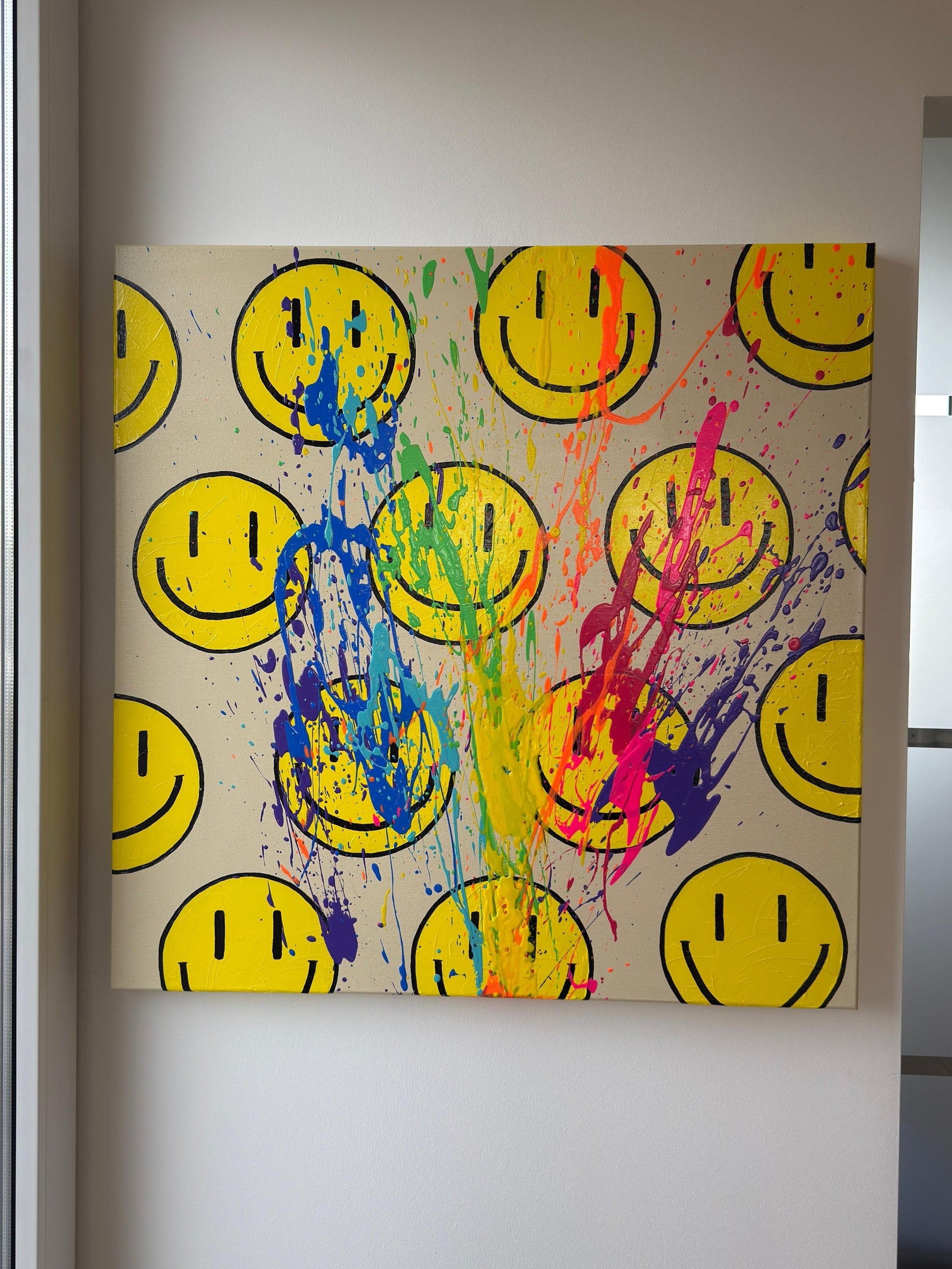 Abstraktes Happy-Face-Acrylbild mit Regenbogen-Farbspritzern auf hellem Hintergrund, moderne Wandkunst mit Struktur in lichtdurchflutetem Raum
