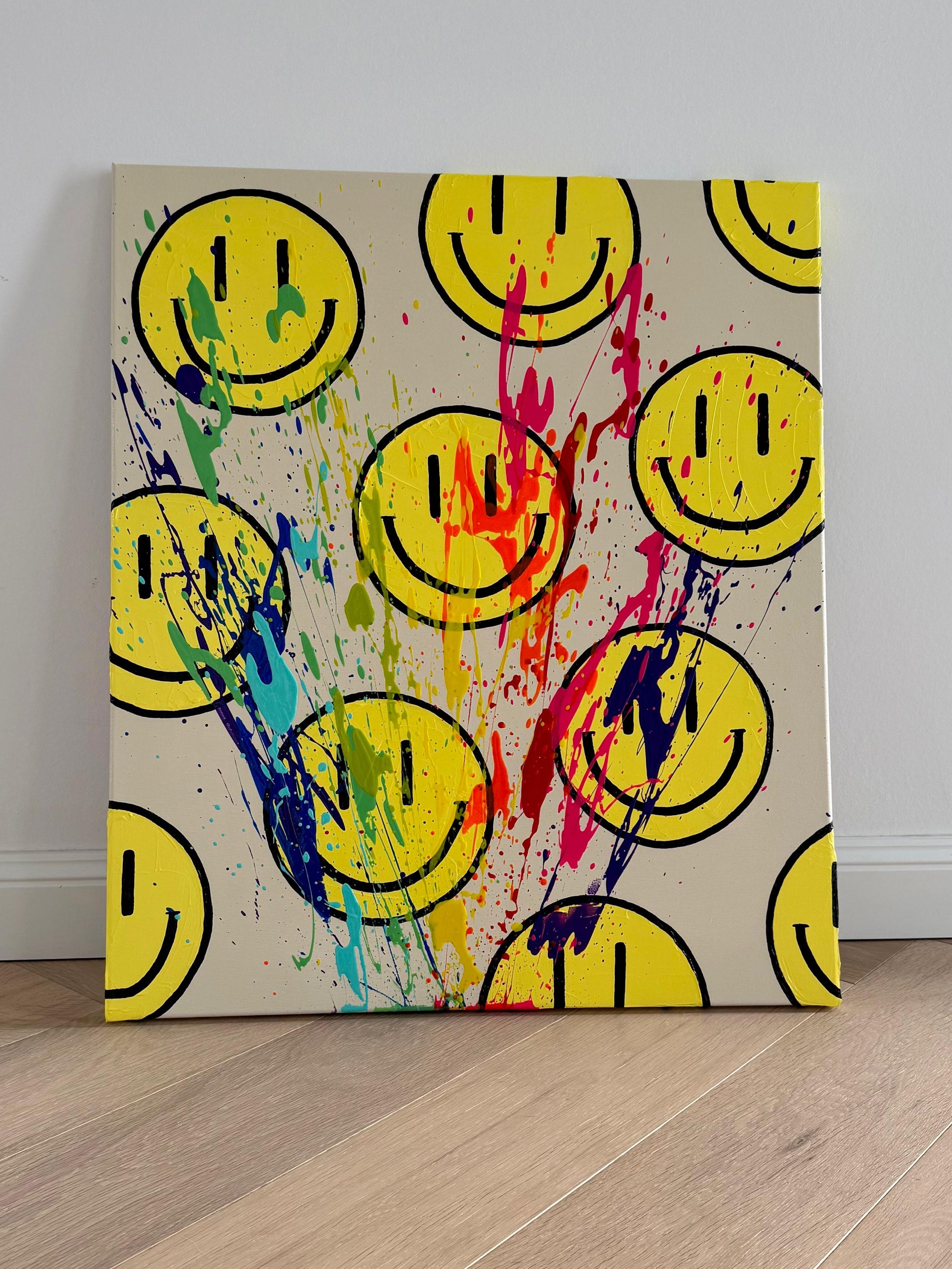 Abstraktes Acrylgemälde „HAPPY #11“ aus der HAPPY Series: gelbe Happy-Face-Motive auf hellem Hintergrund, überzogen von dynamischen Farbspuren in Pink, Blau, Grün und Violett. Das Kunstwerk lehnt ungerahmt an einer weißen Wand auf hellem Holzboden und verbindet grafische Elemente mit freier, expressiver Farbbewegung.