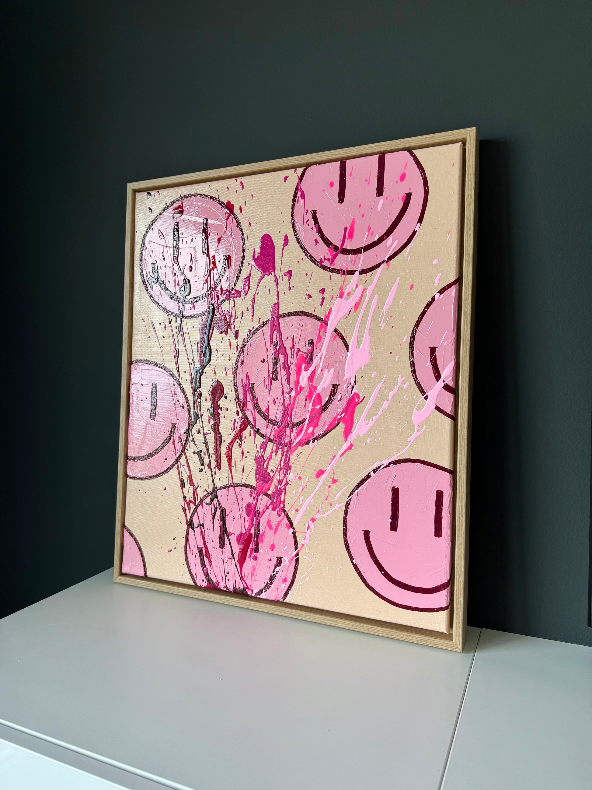 Modernes Smiley Kunstwerk in Rosé und Magenta, abstraktes Acrylbild mit Textur und Farbspritzern, seitliche Perspektive im Raum