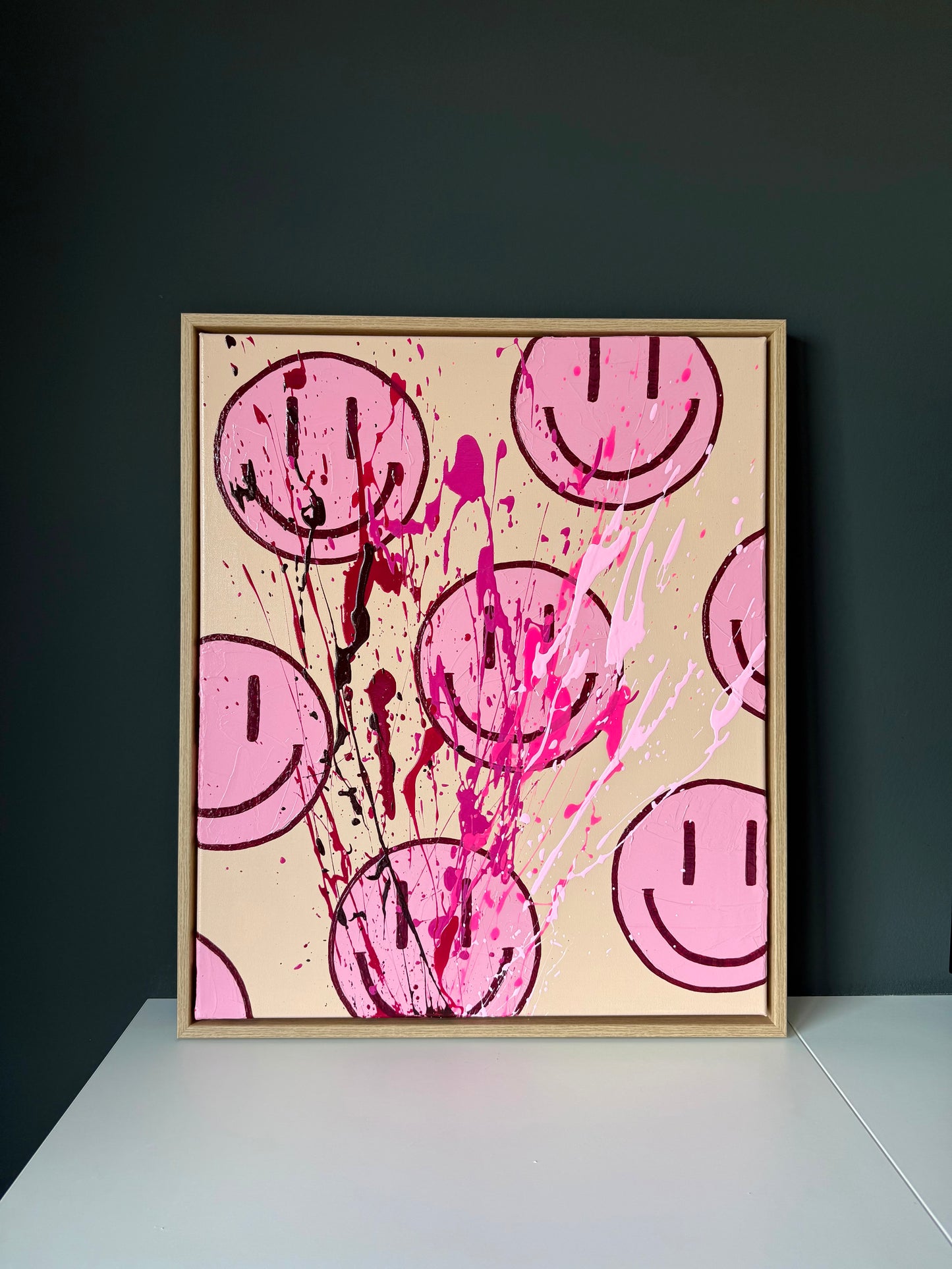 Abstrakte Smiley Kunst auf Leinwand in Beige und Pink, modernes Wandbild im Holzrahmen vor dunkler Wand inszeniert