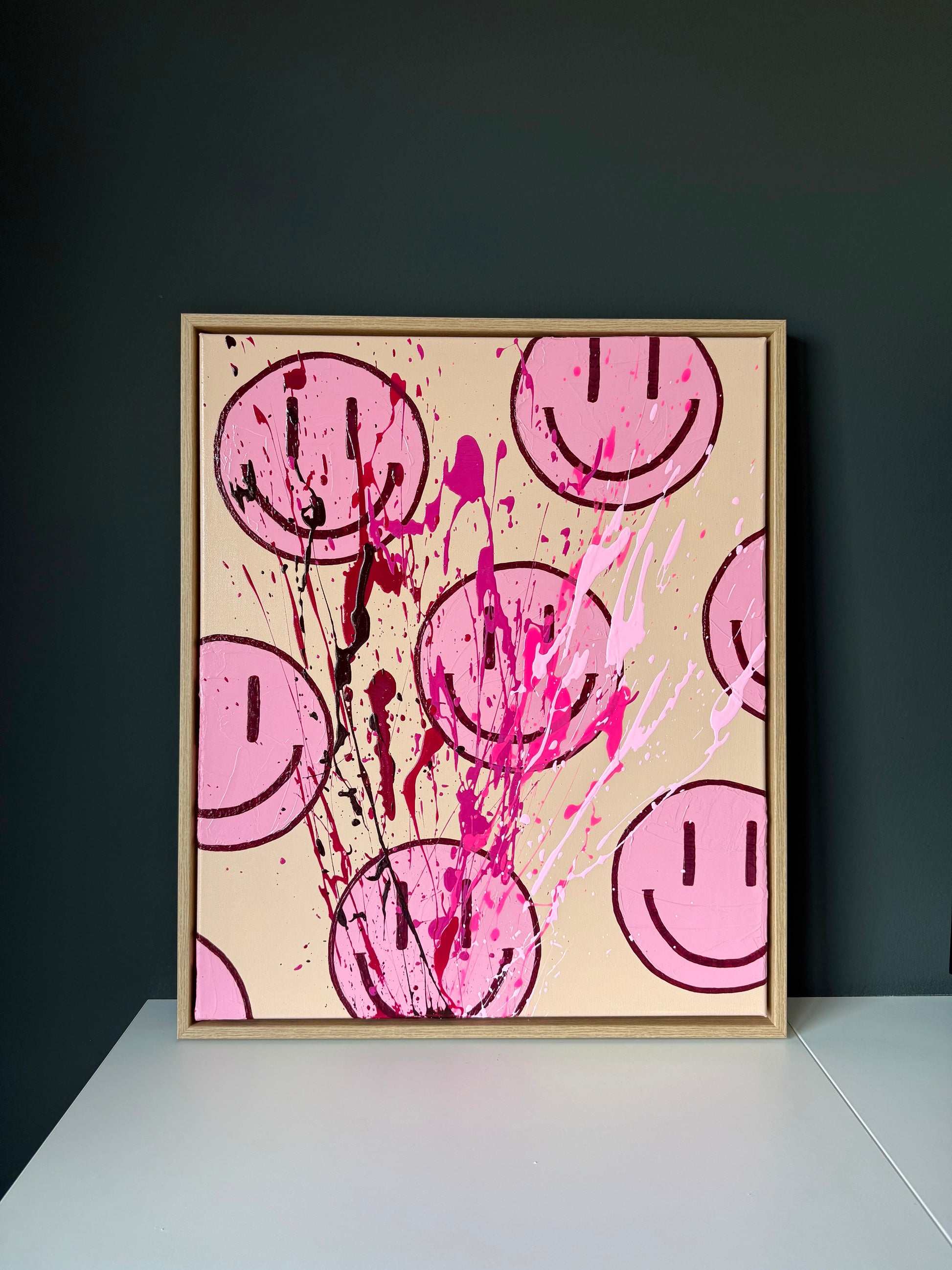 Abstrakte Smiley Kunst auf Leinwand in Beige und Pink, modernes Wandbild im Holzrahmen vor dunkler Wand inszeniert
