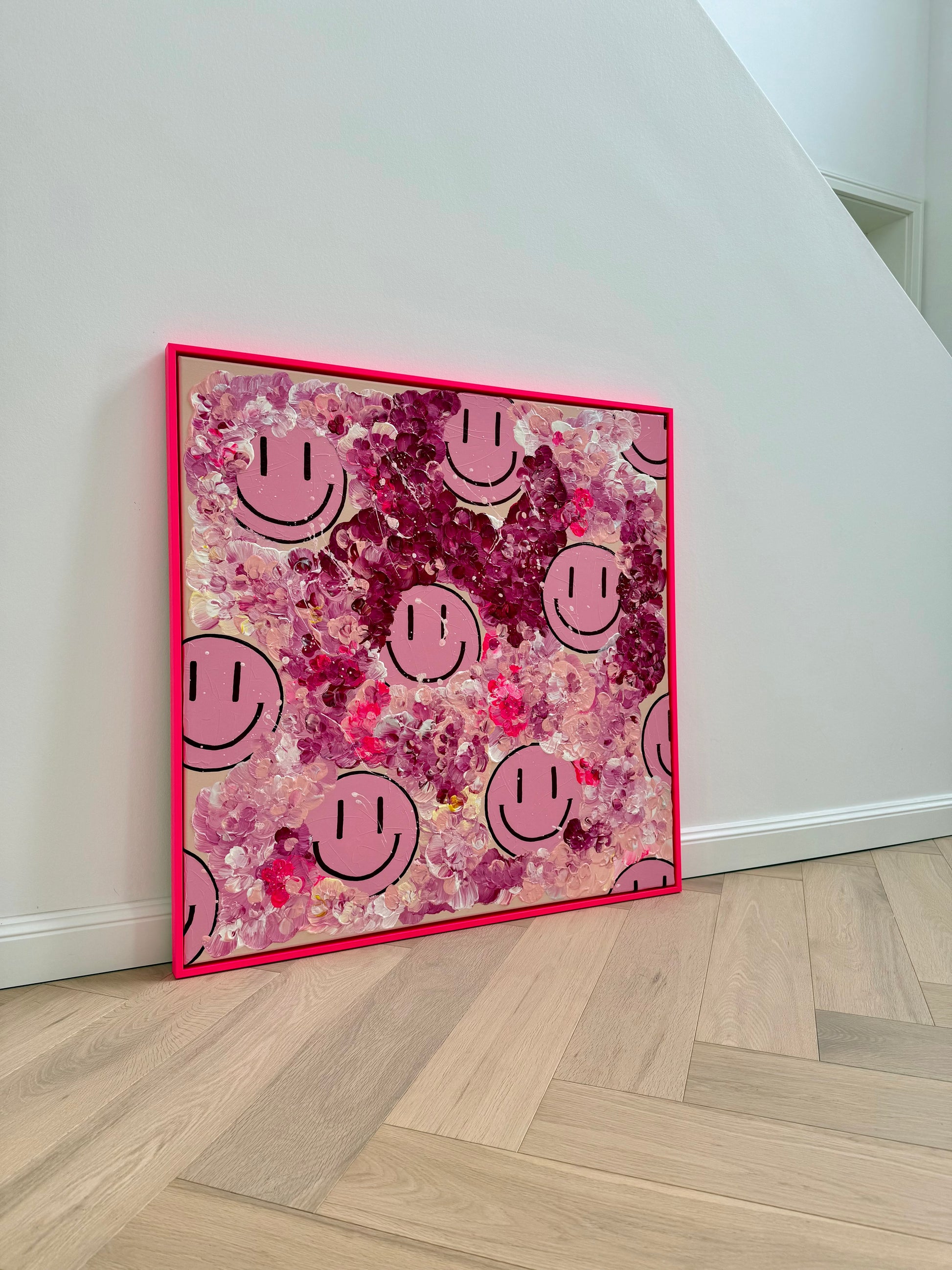 Kunstwerk "HAPPY #20 – FLORALS infused" von Sophia Toschka, pinkes Happy-Face Kunstwerk mit floraler Struktur, abstrakten Blüten und pinkem Rahmen in einem modernen Wohnraum.