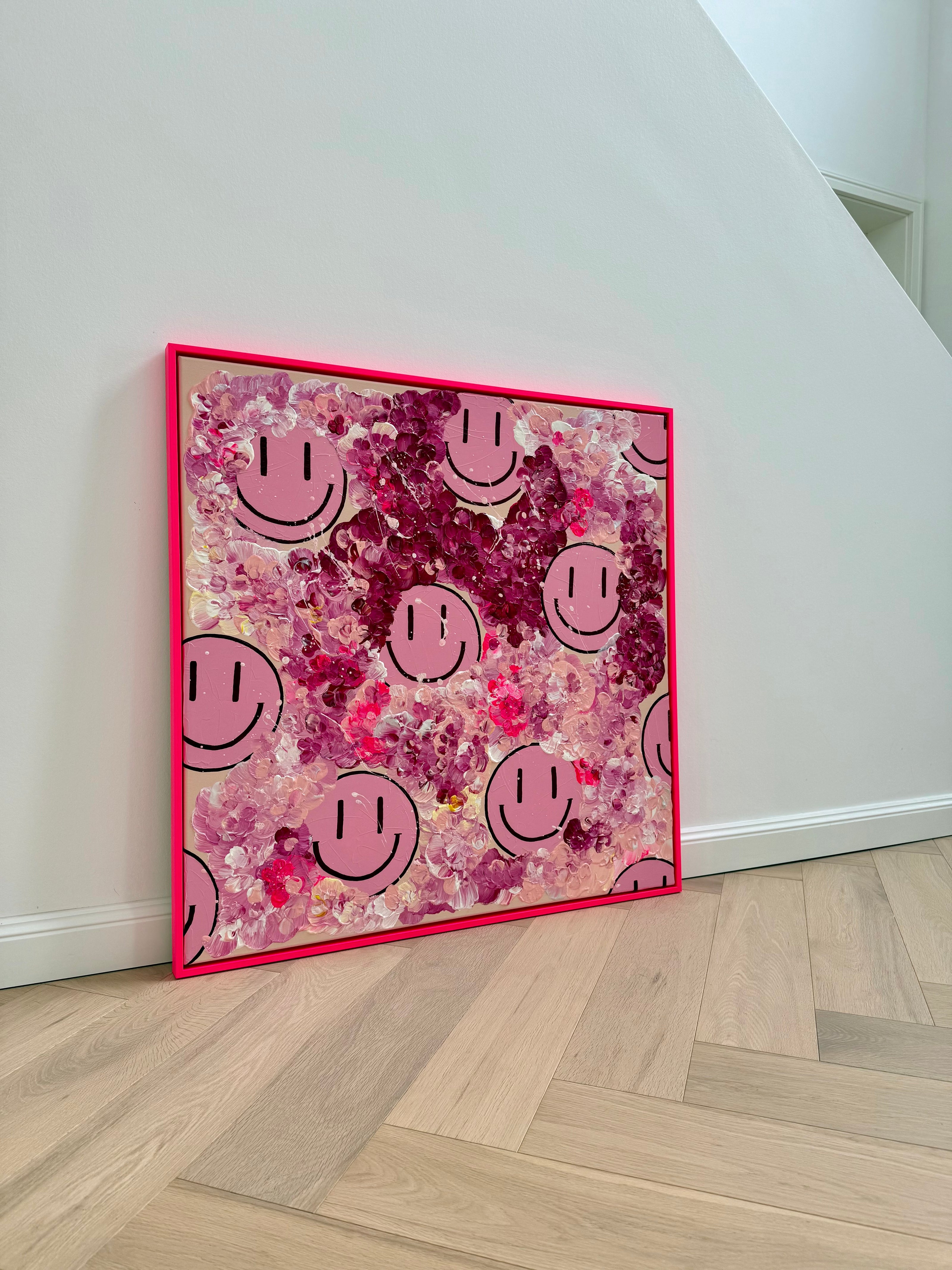 Kunstwerk "HAPPY #20 – FLORALS infused" von Sophia Toschka, pinkes Happy-Face Kunstwerk mit floraler Struktur, abstrakten Blüten und pinkem Rahmen in einem modernen Wohnraum.