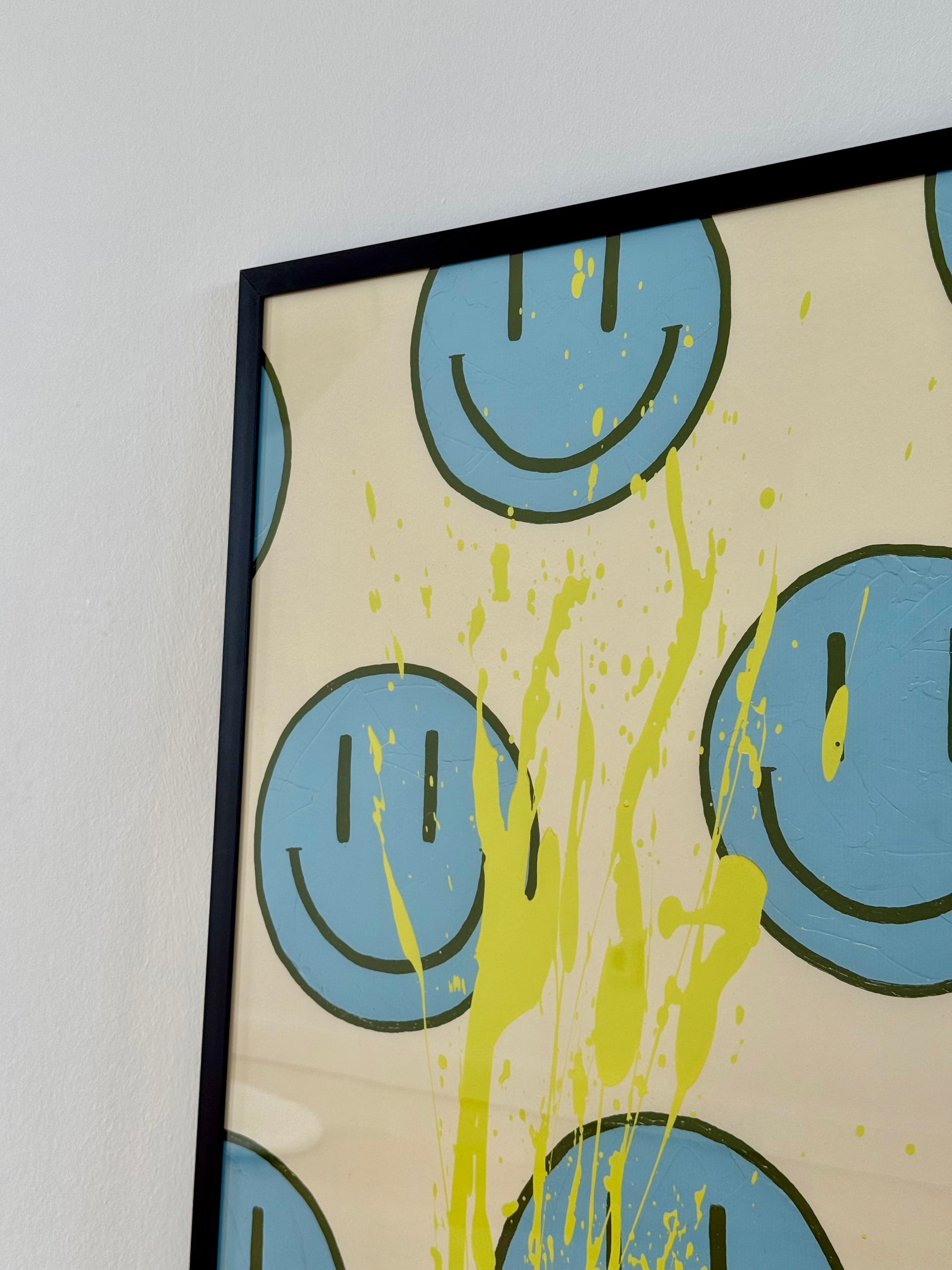 Nahaufnahme von HAPPY #21 mit hellblauen Happy-Faces, olivfarbenen Linien und einem dynamischen zitronengelben Farbspritzer auf Creme.
