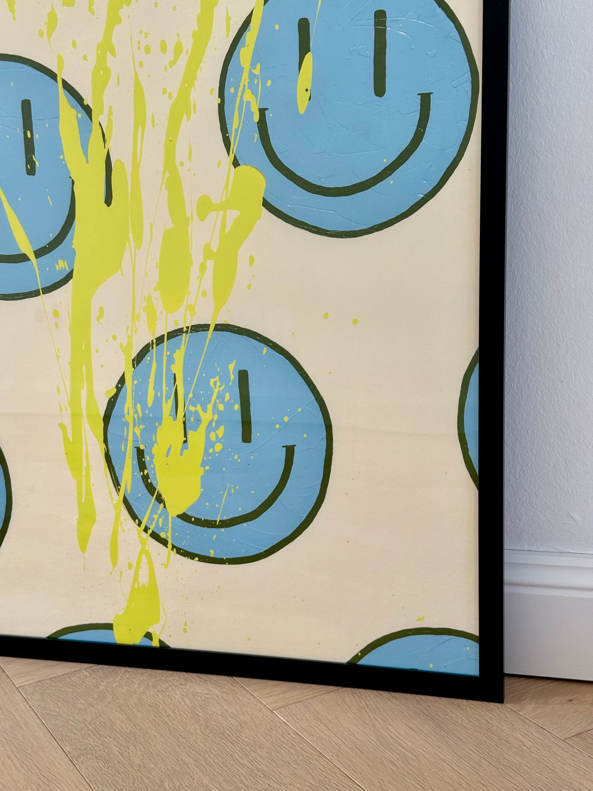 Nahaufnahme der unteren Bildhälfte von HAPPY #21 im schwarzen Rahmen mit hellblauen Happy-Faces, olivfarbenen Konturen und gelben Farbspritzern.