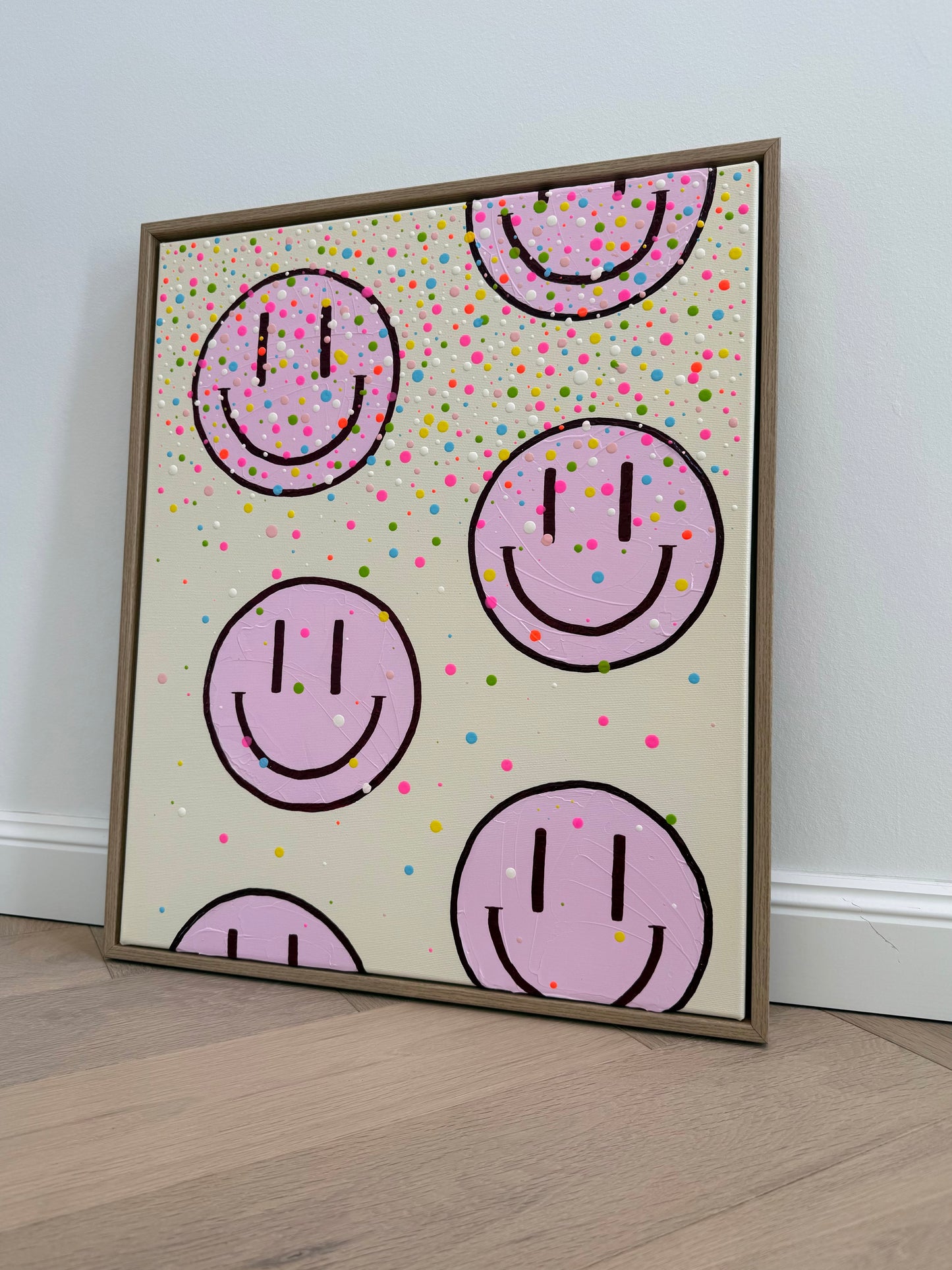 Seitliche Gesamtansicht des Originalkunstwerks HAPPY #26 mit bunten Farbtropfen und hellrosa Happy Faces im Rahmen aus Eiche Natur.