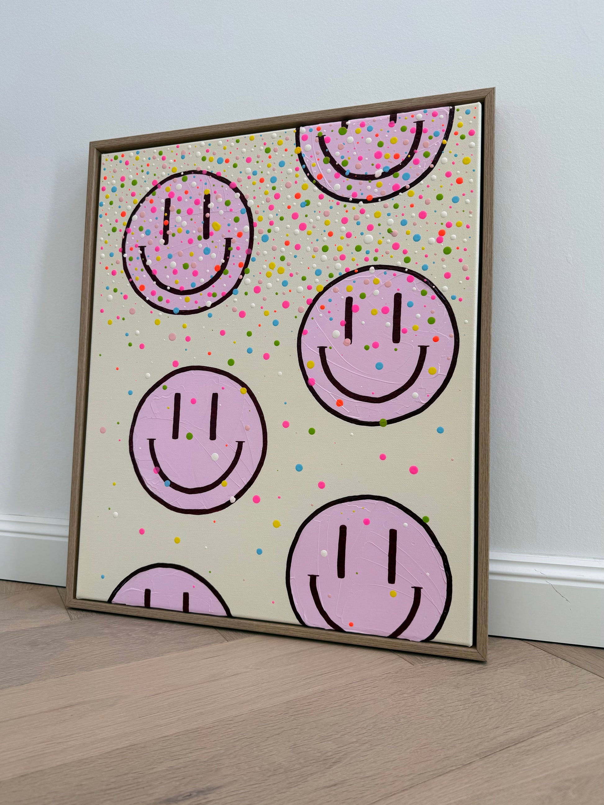 Seitliche Gesamtansicht des Originalkunstwerks HAPPY #26 mit bunten Farbtropfen und hellrosa Happy Faces im Rahmen aus Eiche Natur.