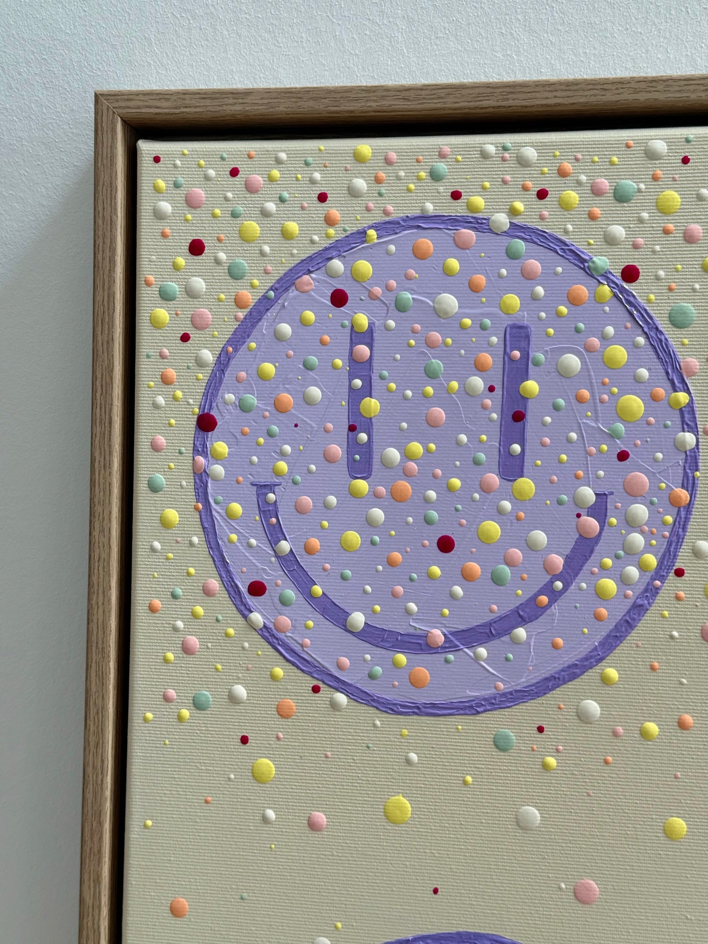 Nahaufnahme eines fliederfarbenen Happy-Faces mit sichtbarer Acrylstruktur und handgesetzten Farbpunkten auf beigem Hintergrund.