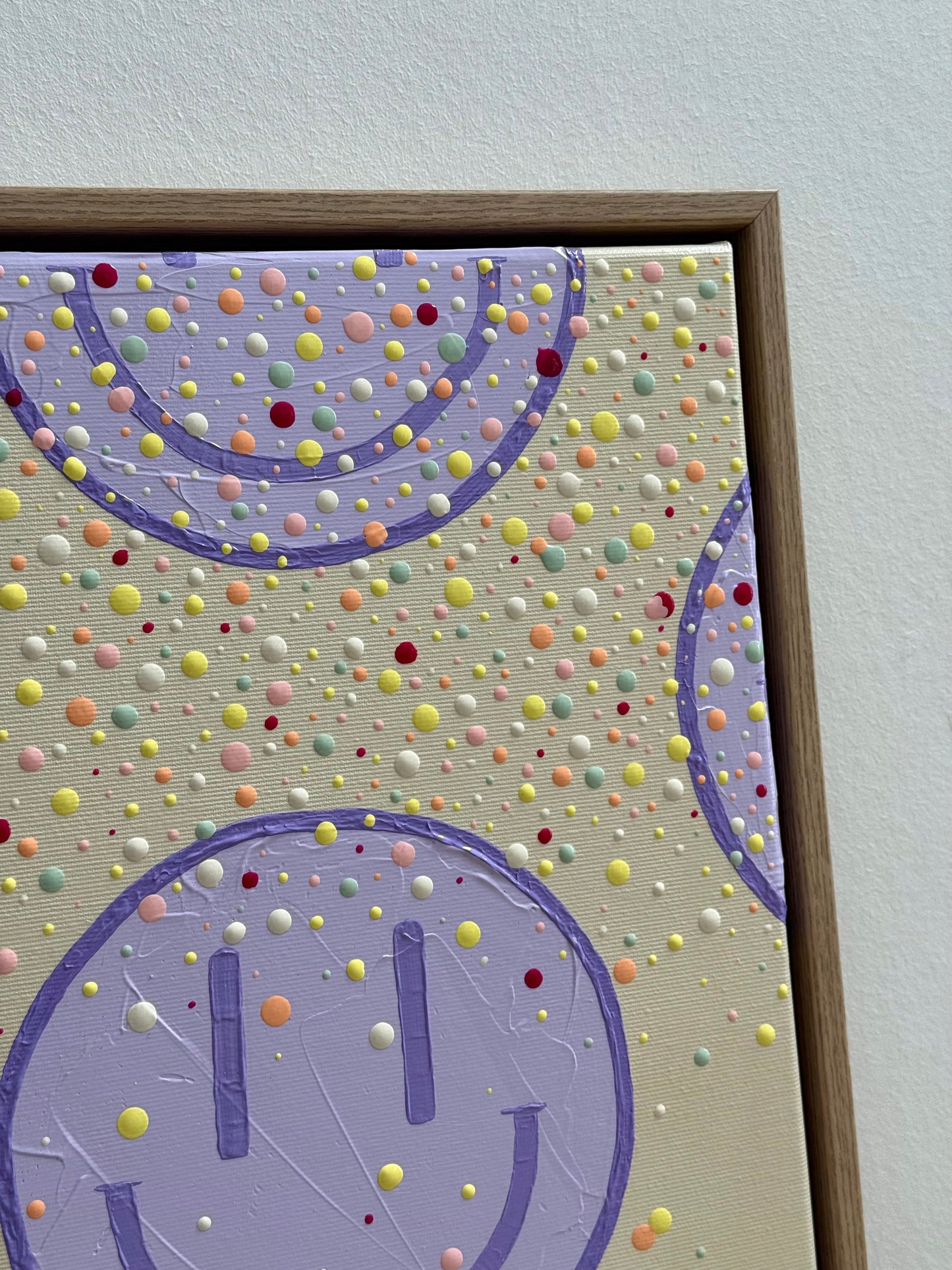 Detailaufnahme eines großen fliederfarbenen Happy-Faces mit zahlreichen erhabenen Farbpunkten und sichtbarer Textur auf Leinwand.