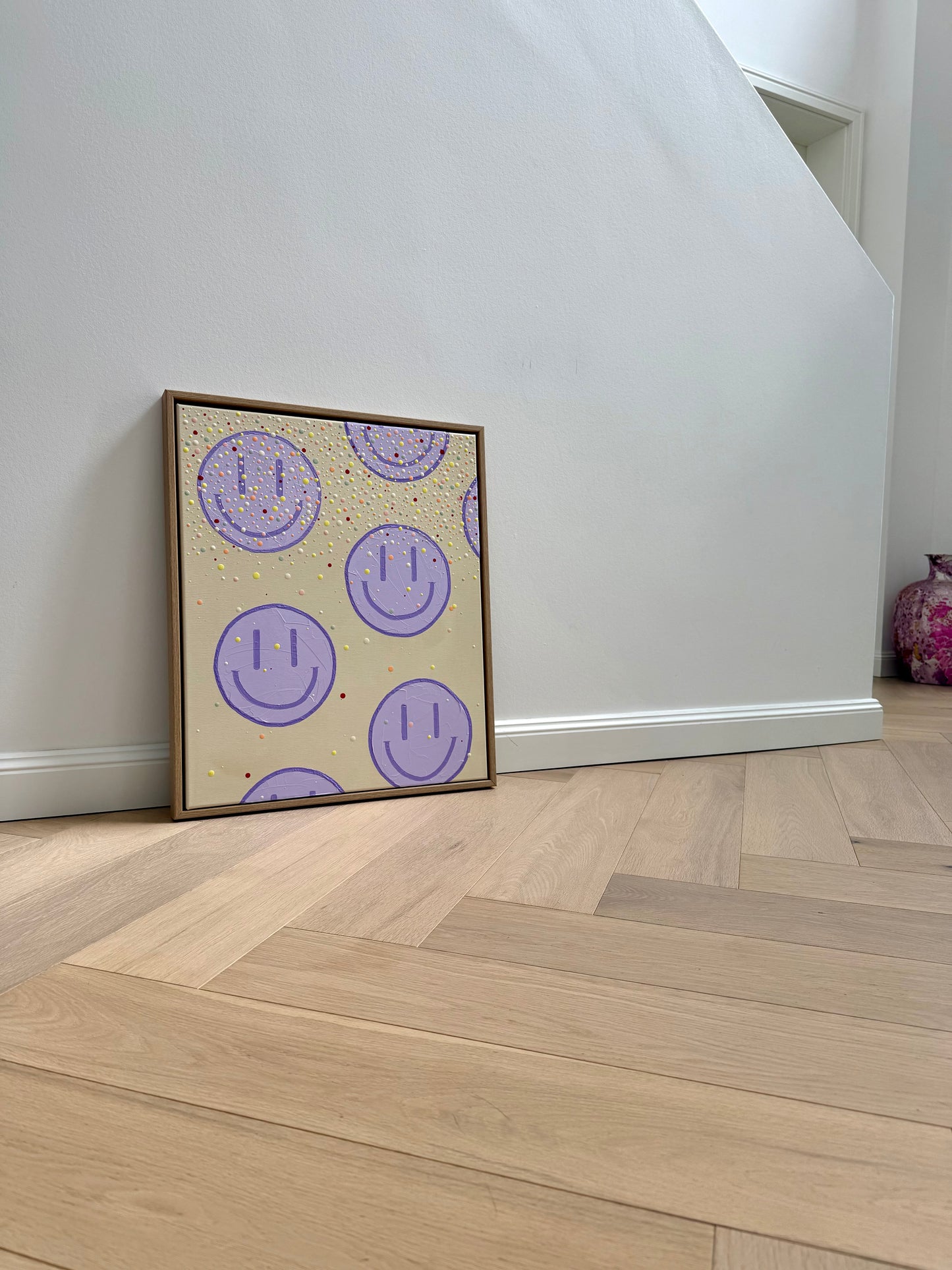 Gerahmtes Originalkunstwerk HAPPY #27 an einer hellen Wand mit natürlichem Holzboden in einem modernen, reduzierten Interior.