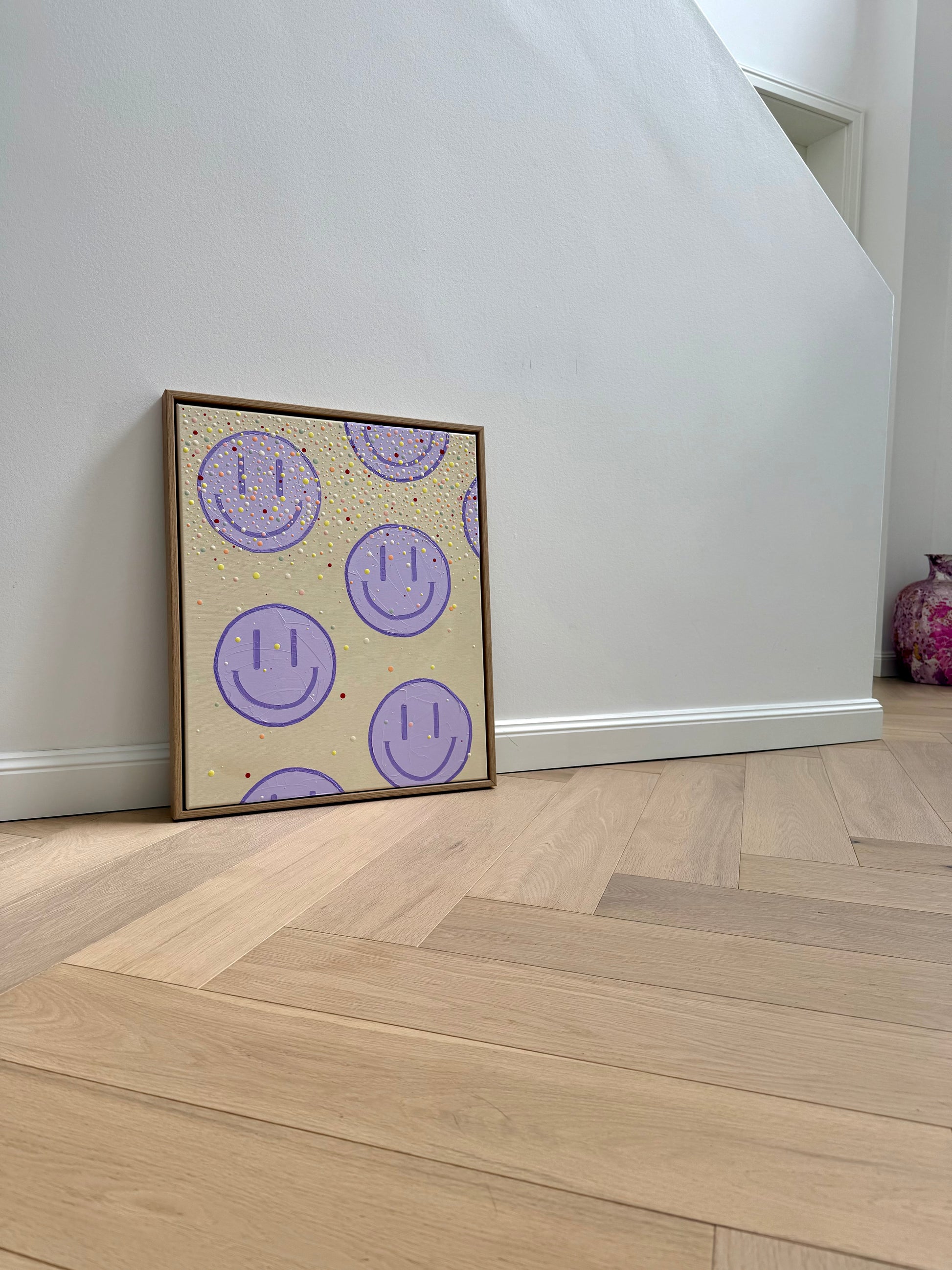 Gerahmtes Originalkunstwerk HAPPY #27 an einer hellen Wand mit natürlichem Holzboden in einem modernen, reduzierten Interior.