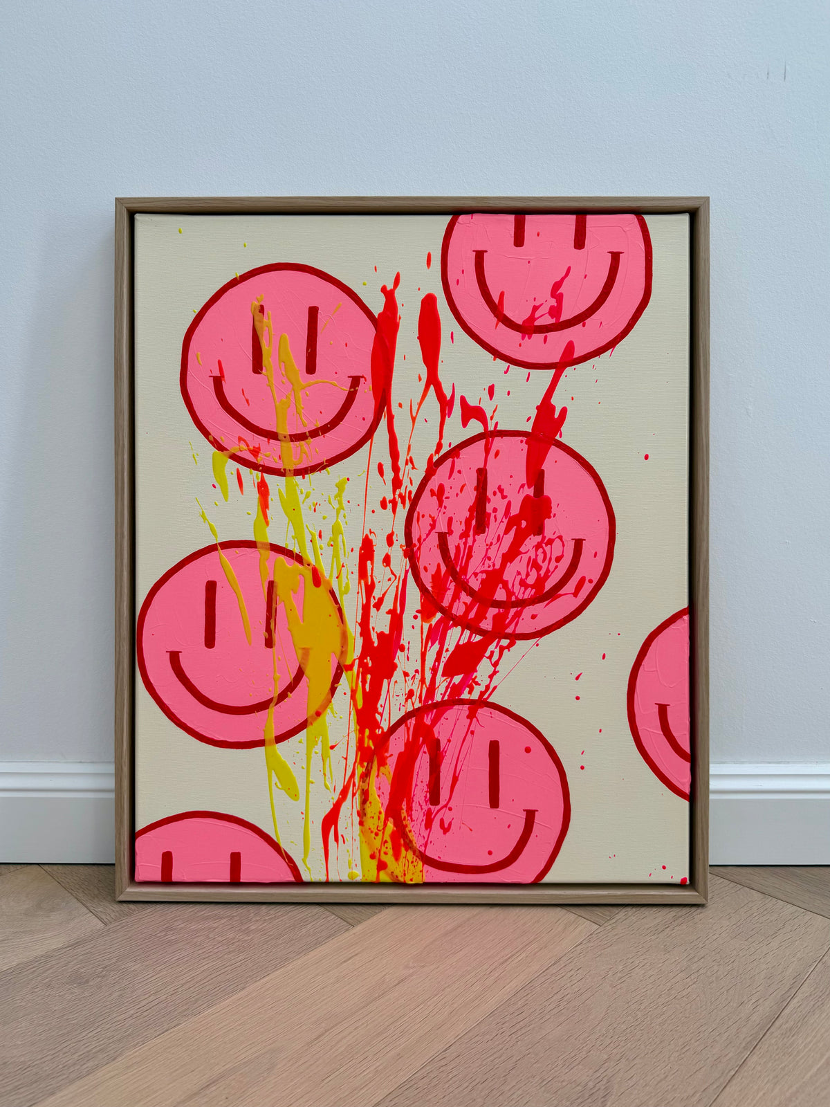 Frontansicht von HAPPY #32 mit pinken Happy Faces und langen, sich überlagernden Farbspuren in Gelb, Neonorange und Neonpink im hellen Eichenrahmen.