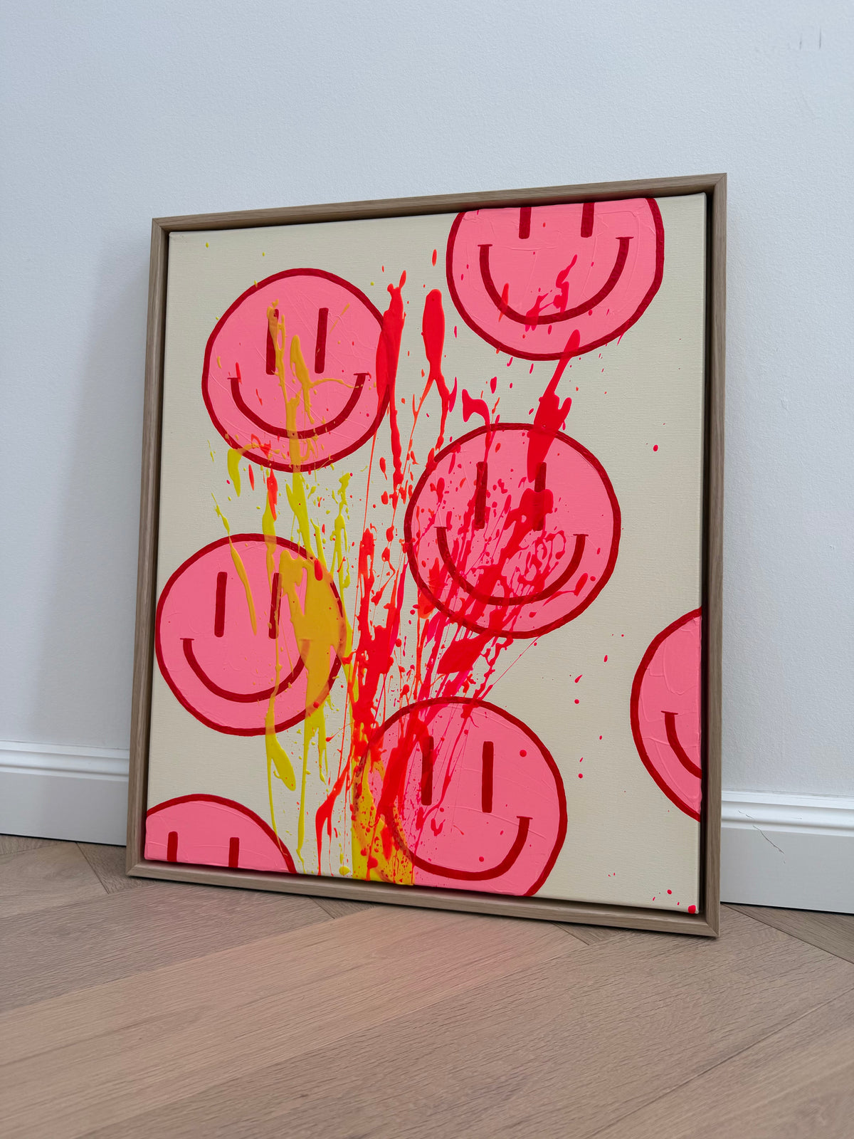 Schrägansicht von HAPPY #32, auf Holzboden an eine helle Wand gelehnt, mit pinken Happy Faces und dynamischen Farbspritzern im Schattenfugenrahmen.