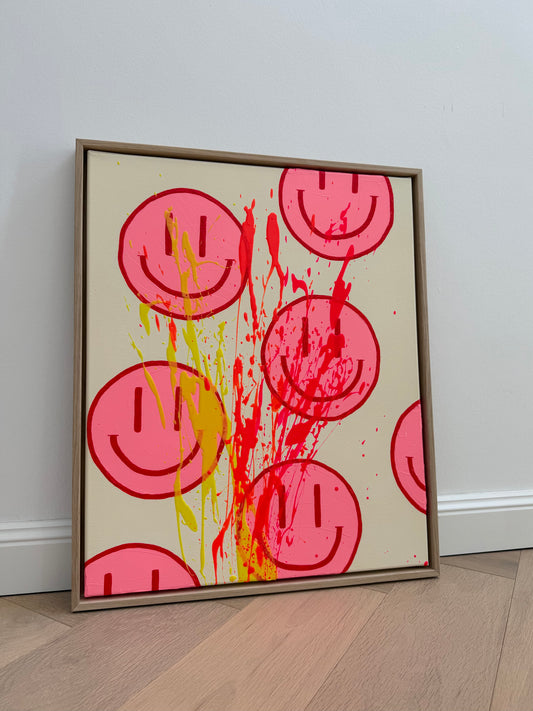 HAPPY #32 mit pinken Happy Faces, kirschroten Konturen und Farbspritzern in Zitronengelb, Neonorange und Neonpink auf beigem Grund, gerahmt in Eiche Natur.