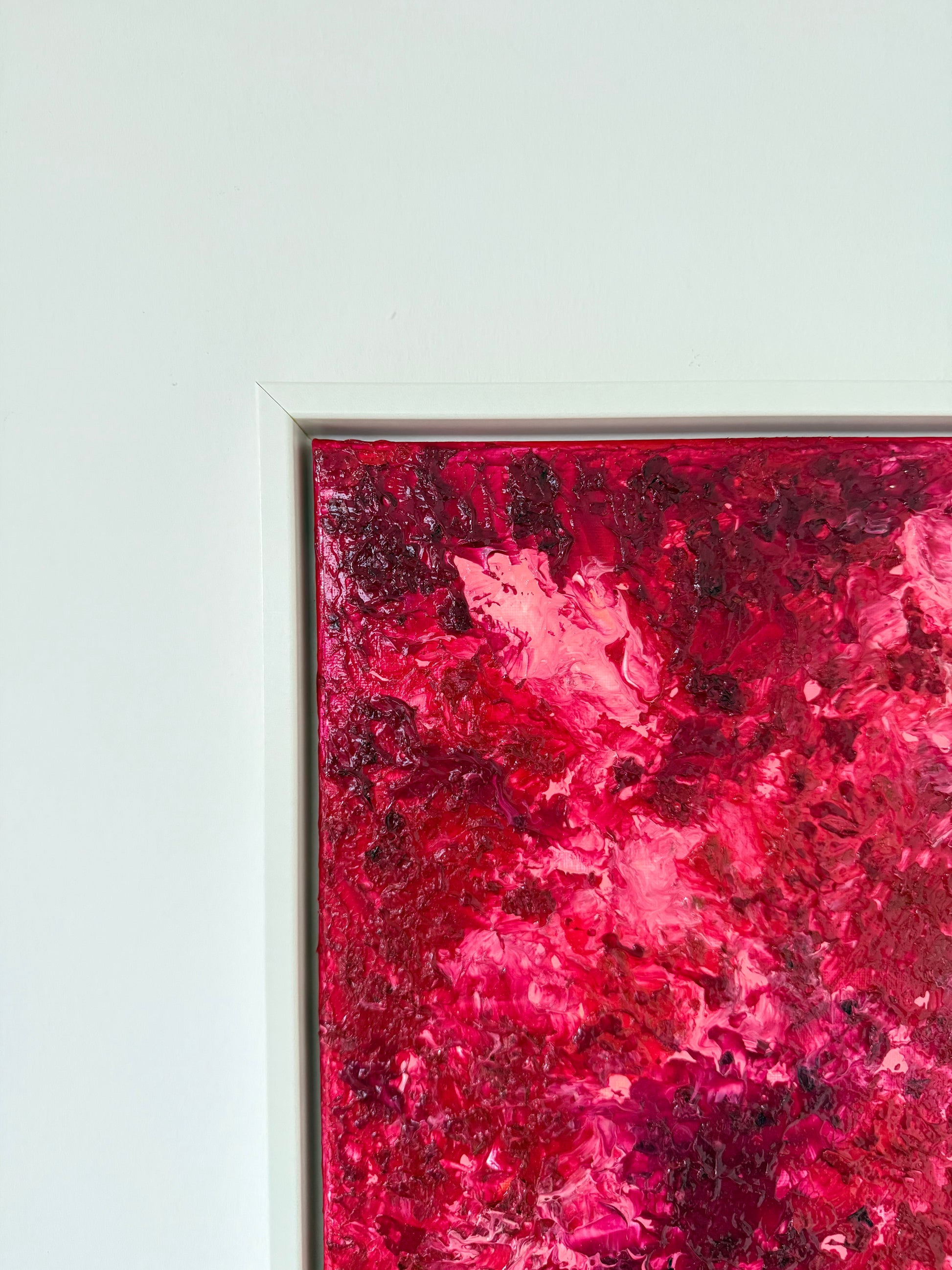 Nahe Aufnahme der oberen Ecke eines abstrakten Kunstwerks in kräftigen Rot- und Pinknuancen, gerahmt in einem weißen Schattenfugenrahmen. Die Bildkante und der Rahmen sind klar sichtbar und zeigen die moderne, hochwertige Präsentation an einer hellen Wand.