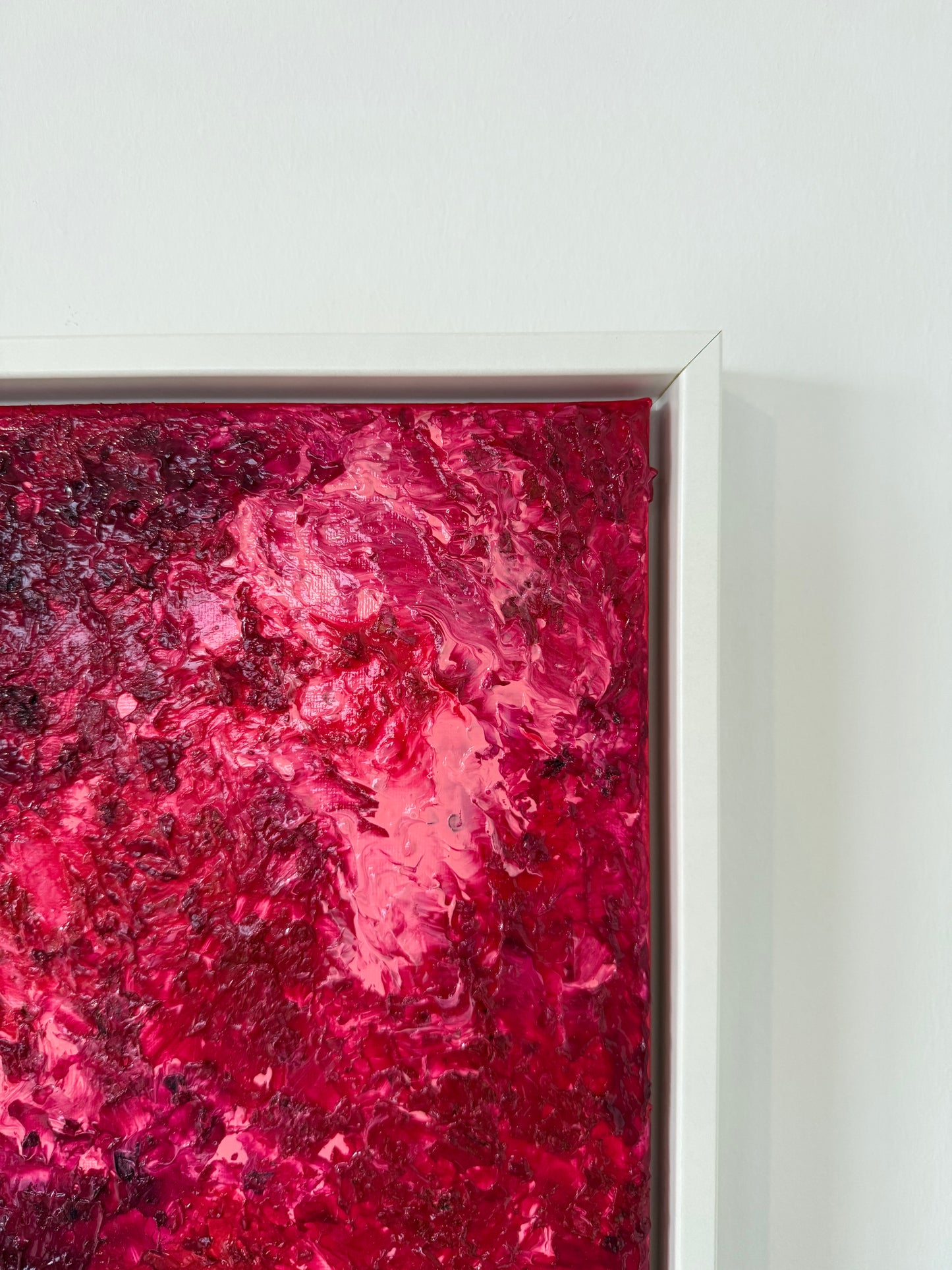 Nahe Aufnahme der oberen rechten Ecke eines abstrakten Kunstwerks in intensiven Rot- und Pinknuancen, eingefasst in einen weißen Schattenfugenrahmen. Die klare Rahmung und die strukturierte Farbfläche zeigen die hochwertige Präsentation an einer hellen Wand.