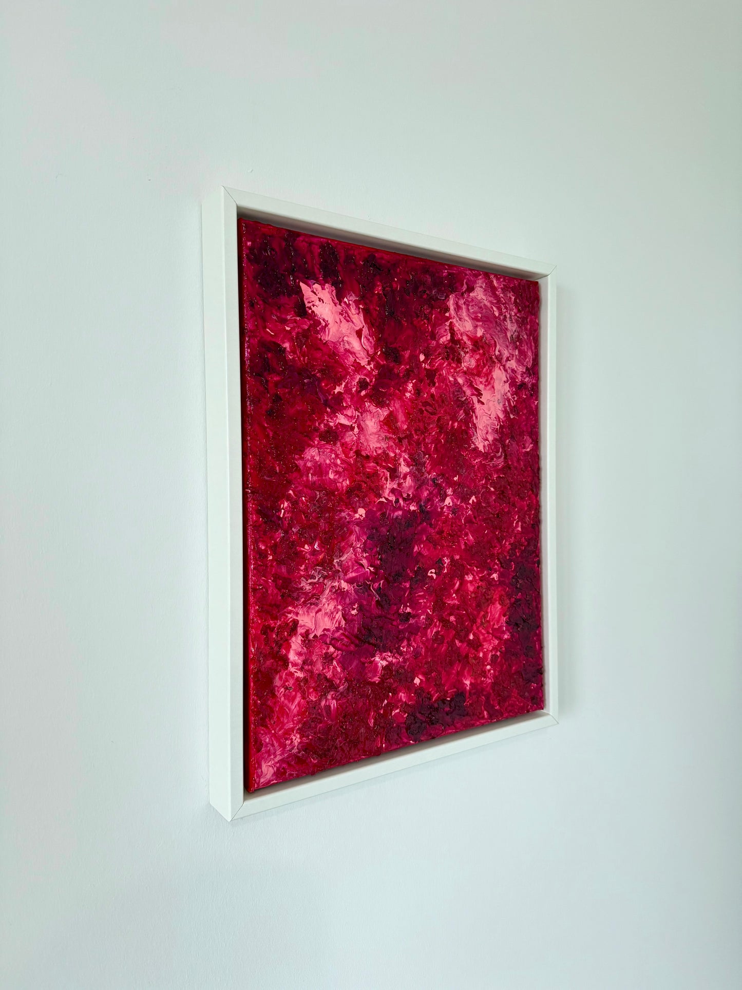 Seitliche Ansicht eines abstrakten Kunstwerks in leuchtenden Rot-, Pink- und Burgundytönen im weißen Schattenfugenrahmen. Die intensiven Farben wirken kraftvoll und setzen einen starken Akzent an der hellen Wand.